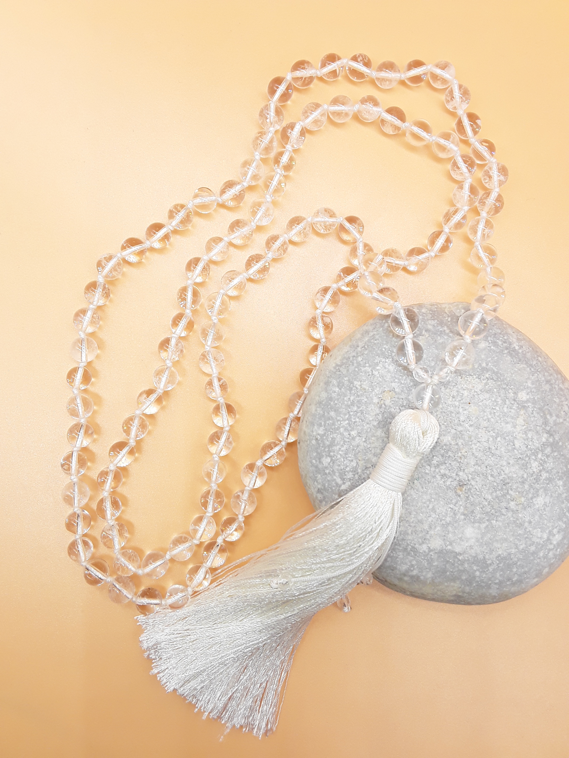 Crystal Quartz Mala Beads with white tassel placed beside white stone on soft background, Polmadeva