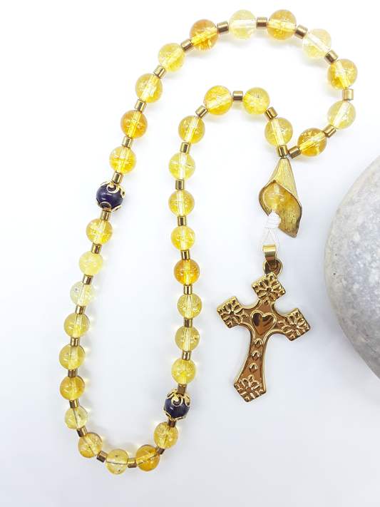 The Quiet Return — Citrine & Amethyst Orthodox Rosary by Polmadeva, citrine and amethyst beads with hematite spacers and stainless steel cross, photographed beside natural stone to emphasize grounded repetition and inward prayer.
