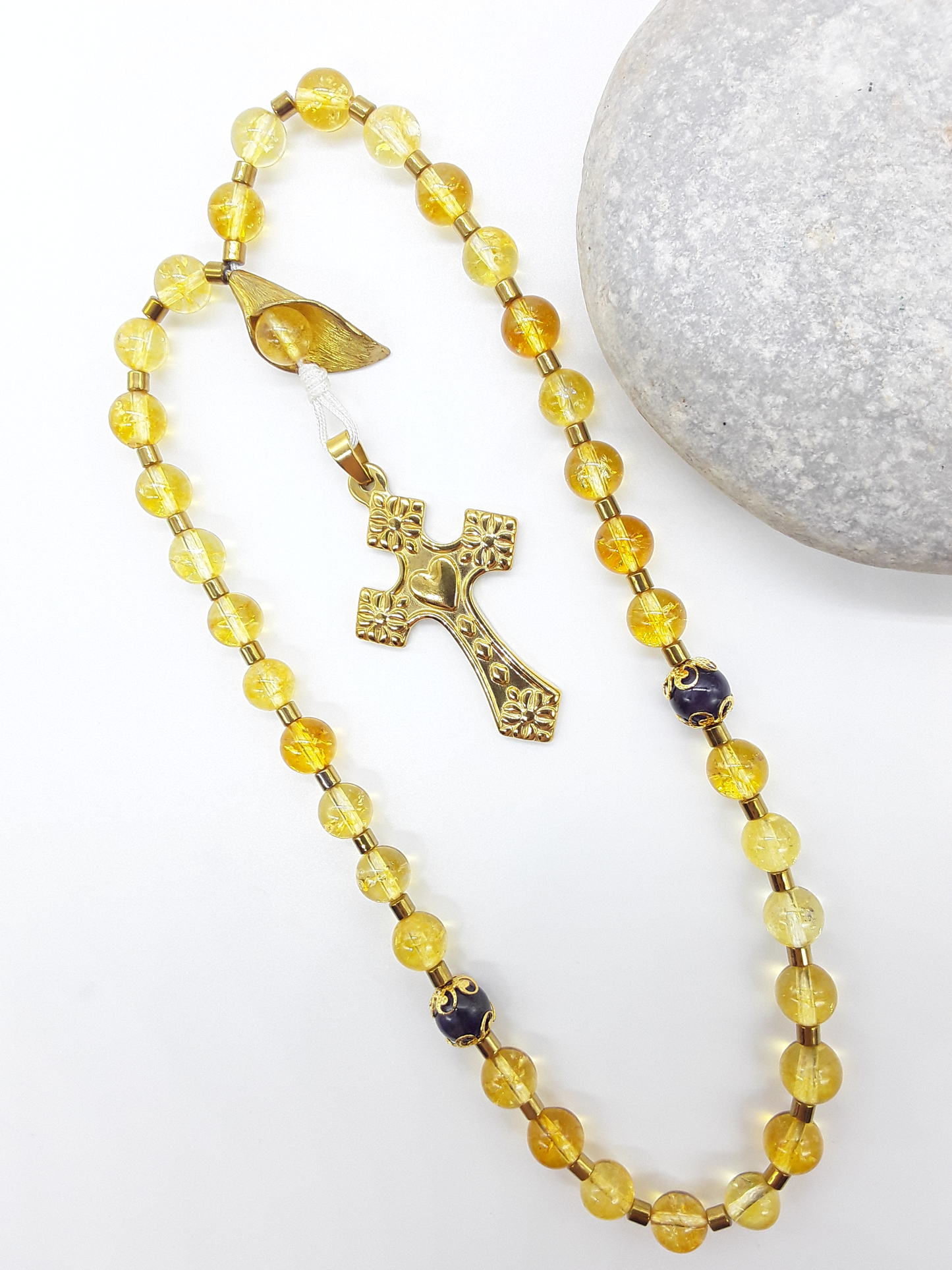 The Quiet Return — Citrine & Amethyst Orthodox Rosary by Polmadeva, citrine and amethyst beads with hematite spacers and stainless steel cross, photographed beside natural stone to emphasize grounded repetition and inward prayer.