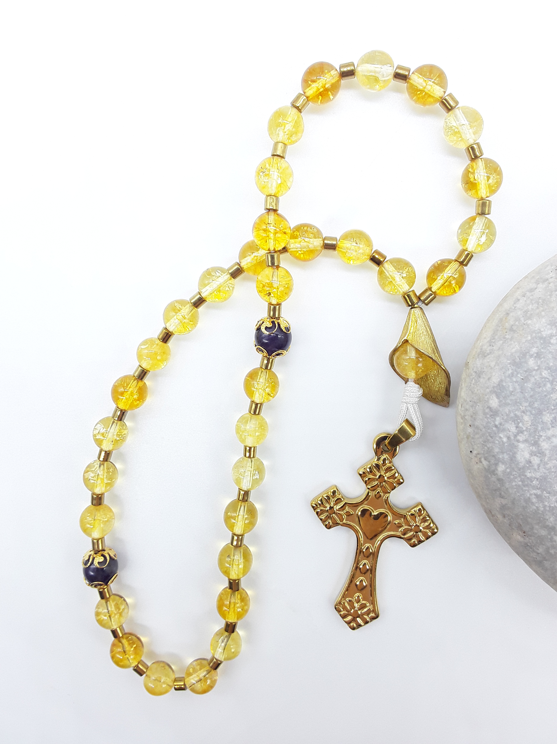 The Quiet Return — Citrine & Amethyst Orthodox Rosary by Polmadeva, citrine and amethyst beads with hematite spacers and stainless steel cross, photographed beside natural stone to emphasize grounded repetition and inward prayer.