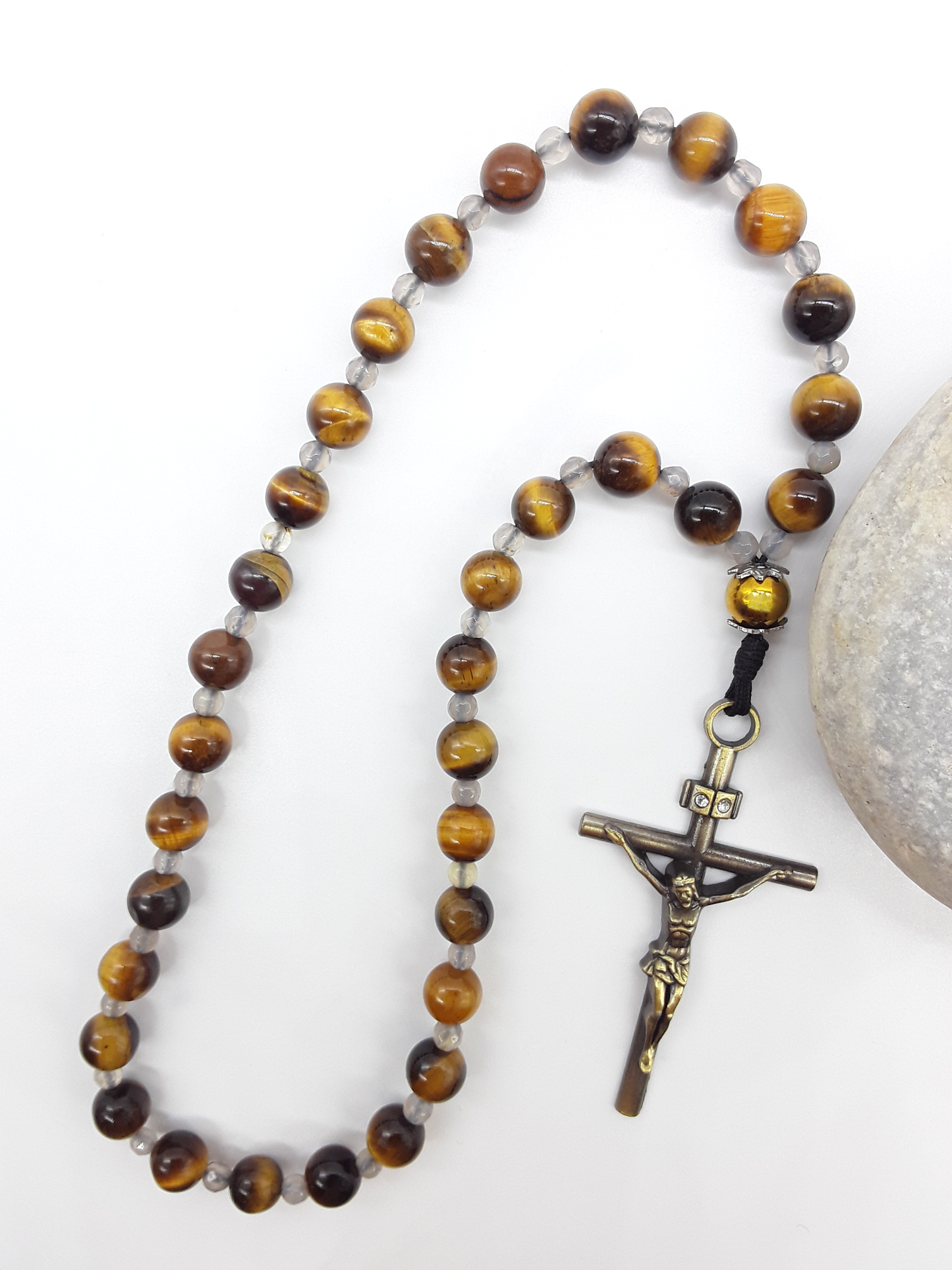 The Quiet Return — Tiger’s Eye Orthodox Rosary by Polmadeva, Tiger’s Eye and Hematite beads with Agate spacers and a bronze zircon cross, photographed beside natural stone to emphasize balance, clarity, and grounded prayer.