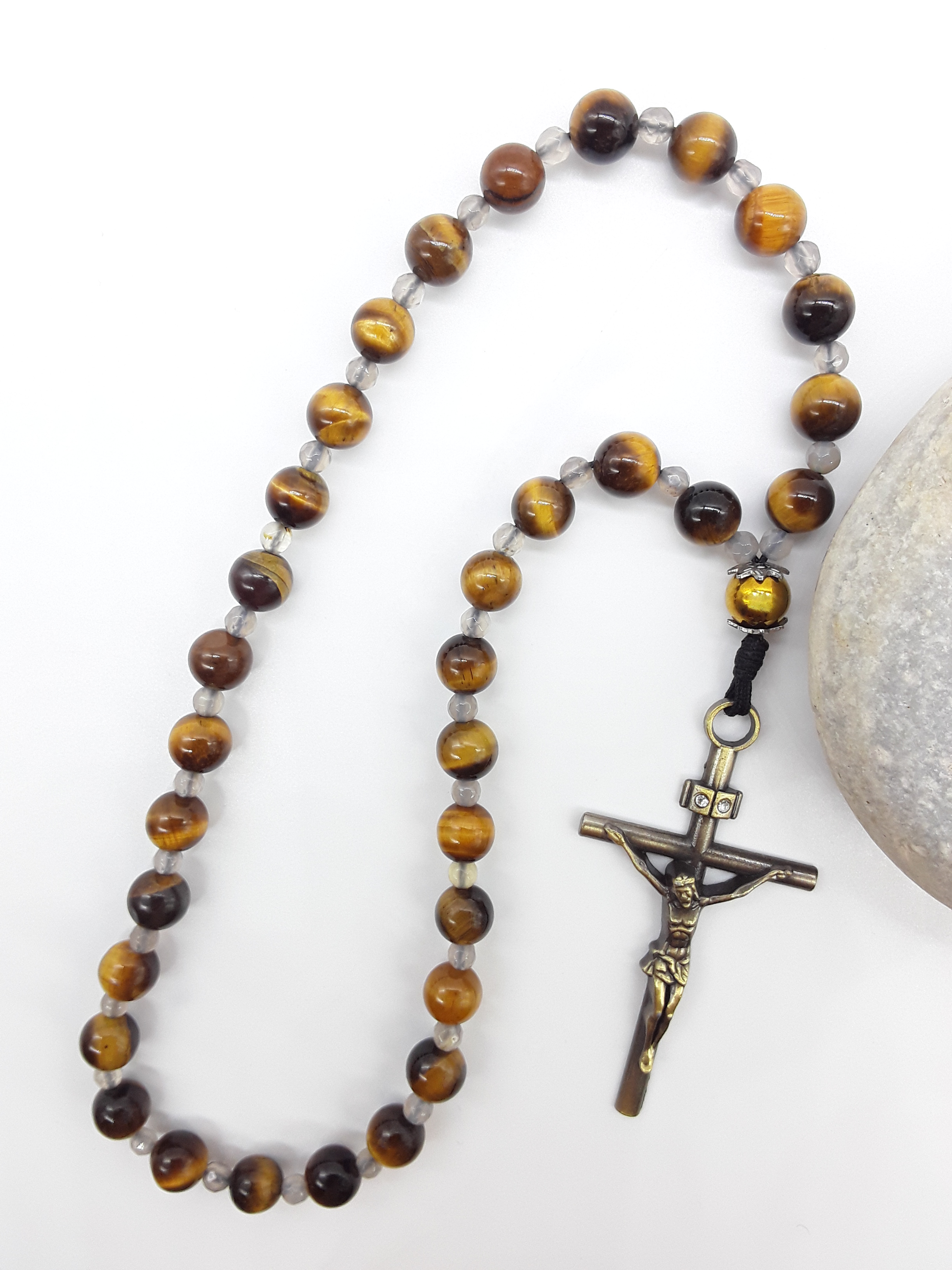 The Quiet Return — Tiger’s Eye Orthodox Rosary by Polmadeva, Tiger’s Eye and Hematite beads with Agate spacers and a bronze zircon cross, photographed beside natural stone to emphasize balance, clarity, and grounded prayer.