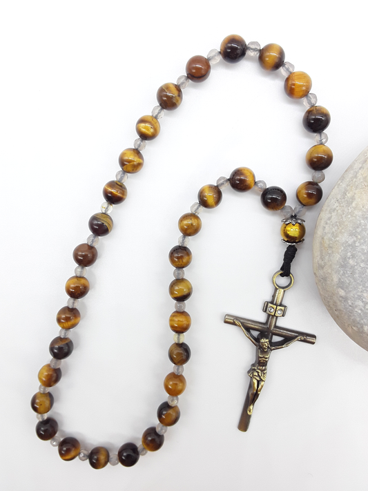 The Quiet Return — Tiger’s Eye Orthodox Rosary by Polmadeva, Tiger’s Eye and Hematite beads with Agate spacers and a bronze zircon cross, photographed beside natural stone to emphasize balance, clarity, and grounded prayer.