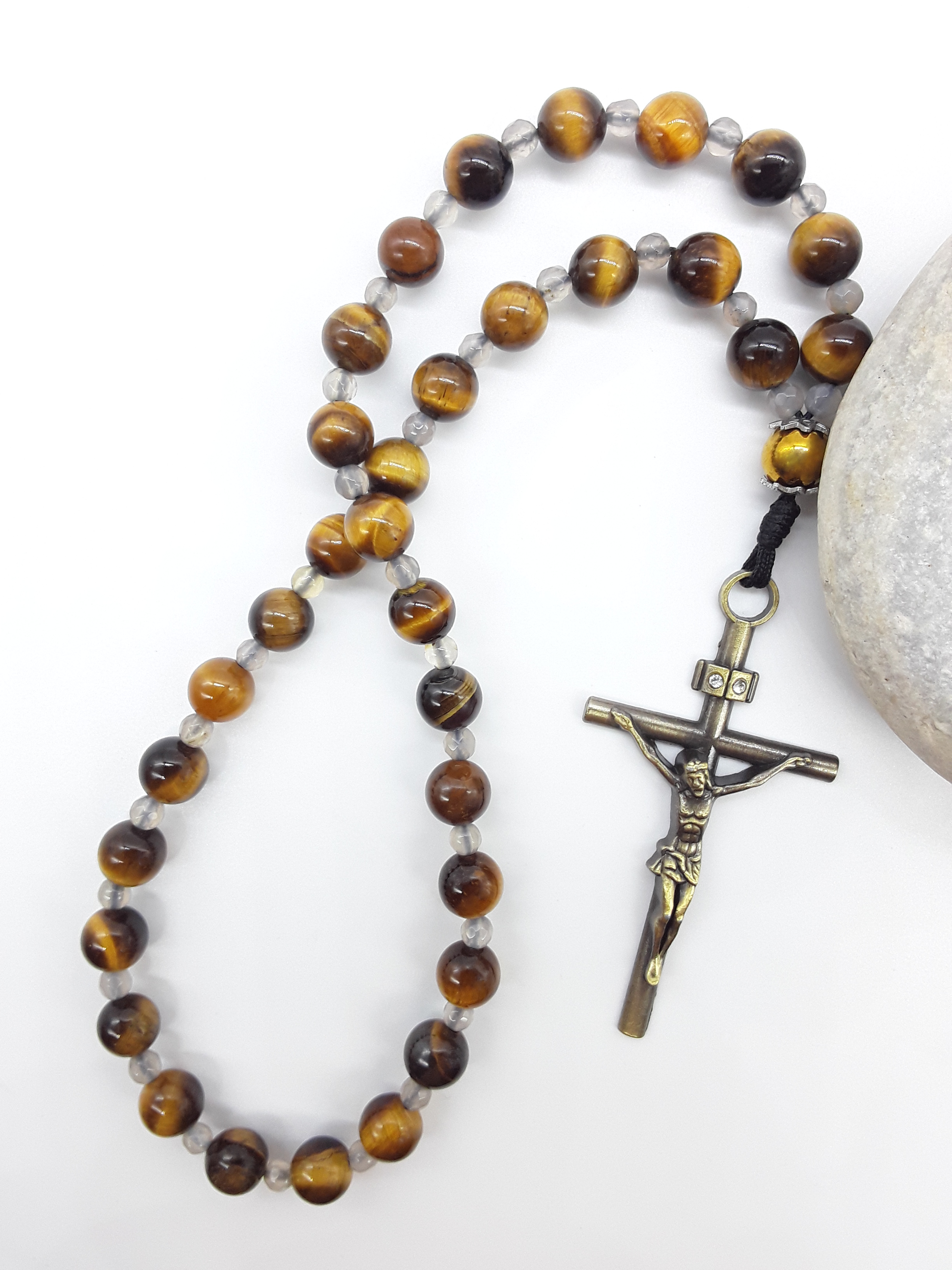 The Quiet Return — Tiger’s Eye Orthodox Rosary by Polmadeva, Tiger’s Eye and Hematite beads with Agate spacers and a bronze zircon cross, photographed beside natural stone to emphasize balance, clarity, and grounded prayer.