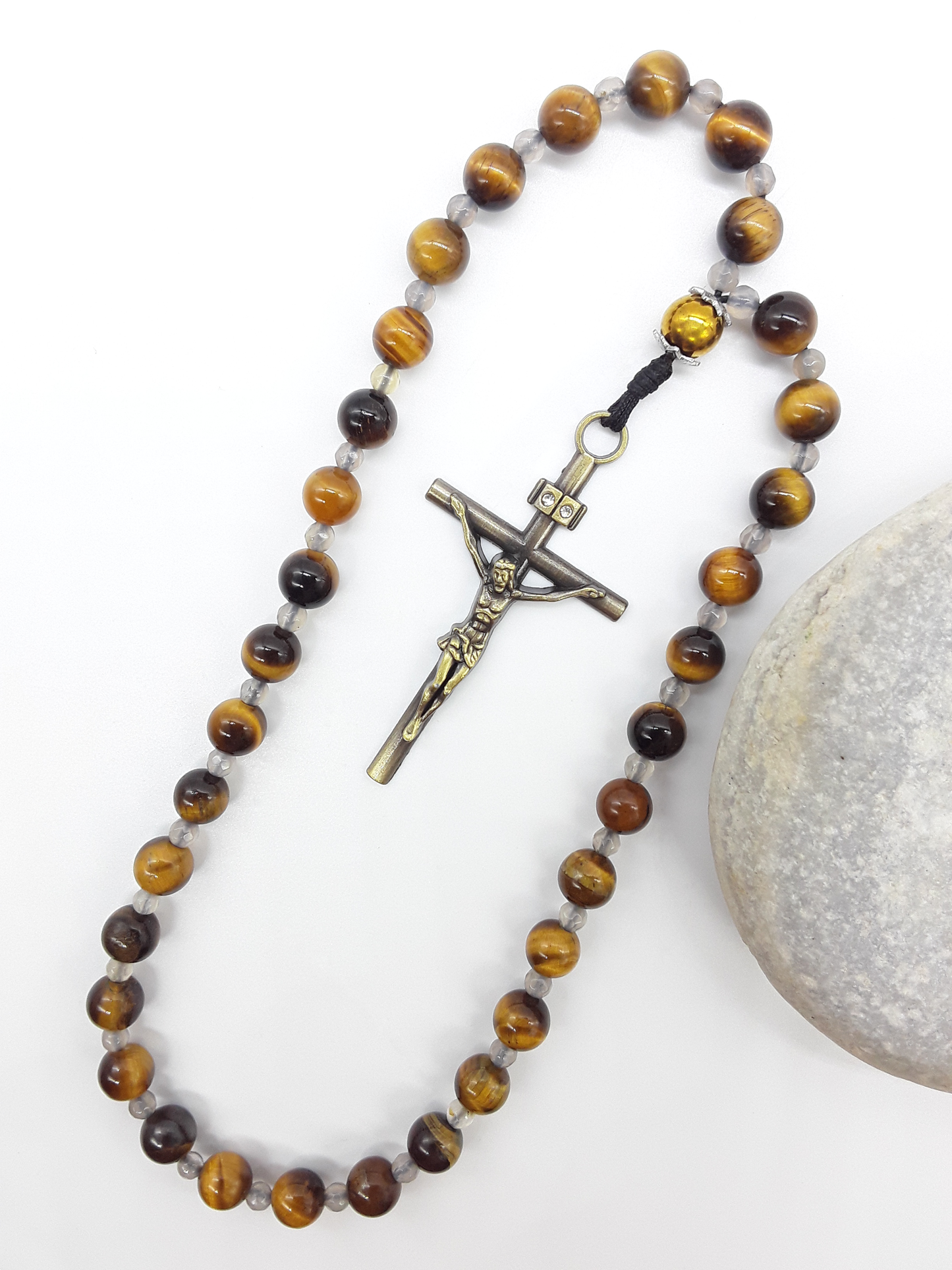 The Quiet Return — Tiger’s Eye Orthodox Rosary by Polmadeva, Tiger’s Eye and Hematite beads with Agate spacers and a bronze zircon cross, photographed beside natural stone to emphasize balance, clarity, and grounded prayer.