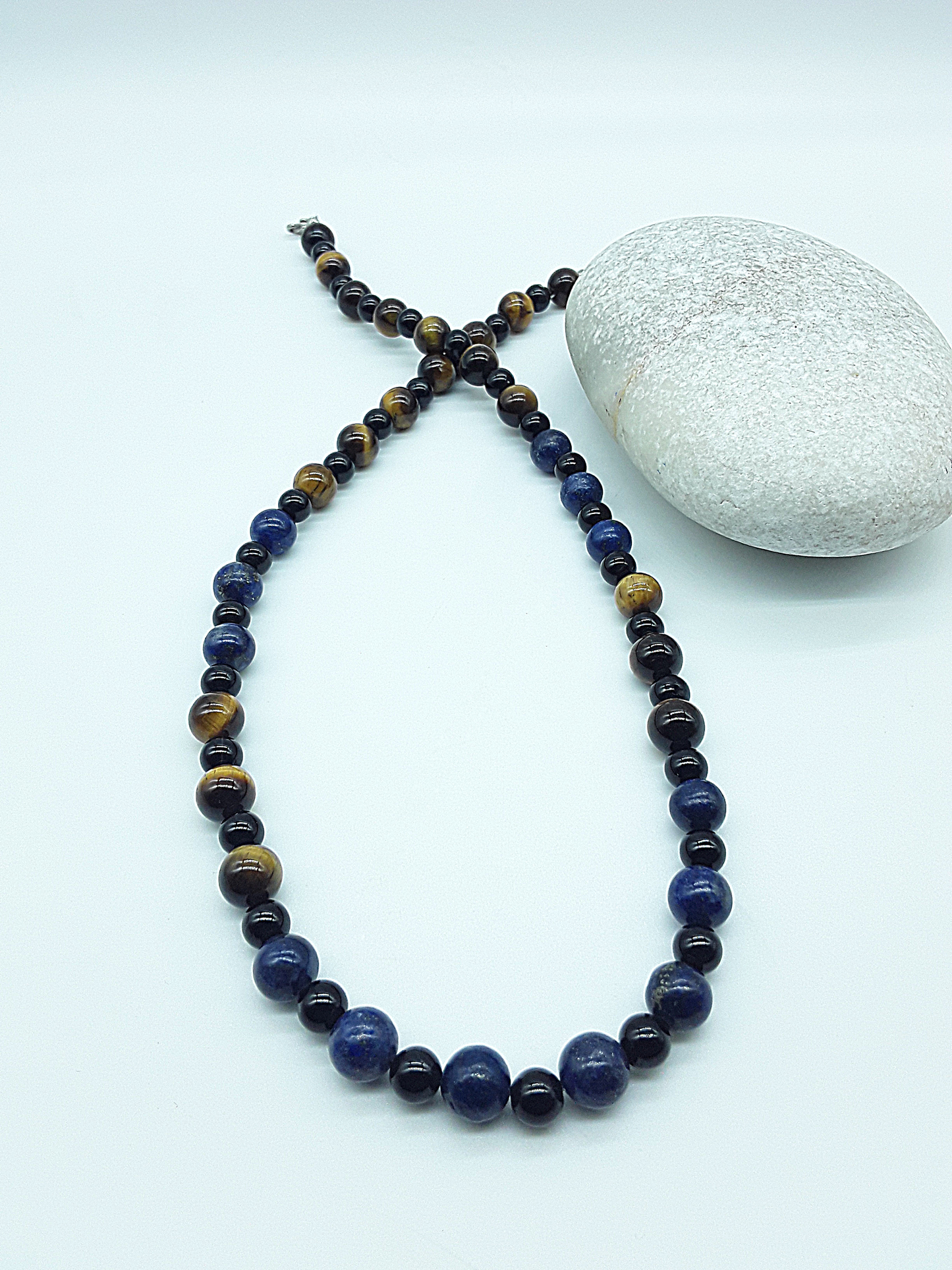 Polmadeva Quiet Sentinel Necklace with lapis lazuli, tiger’s eye and black onyx beads arranged in crossed composition beside natural stone, Guardian Spirit collection