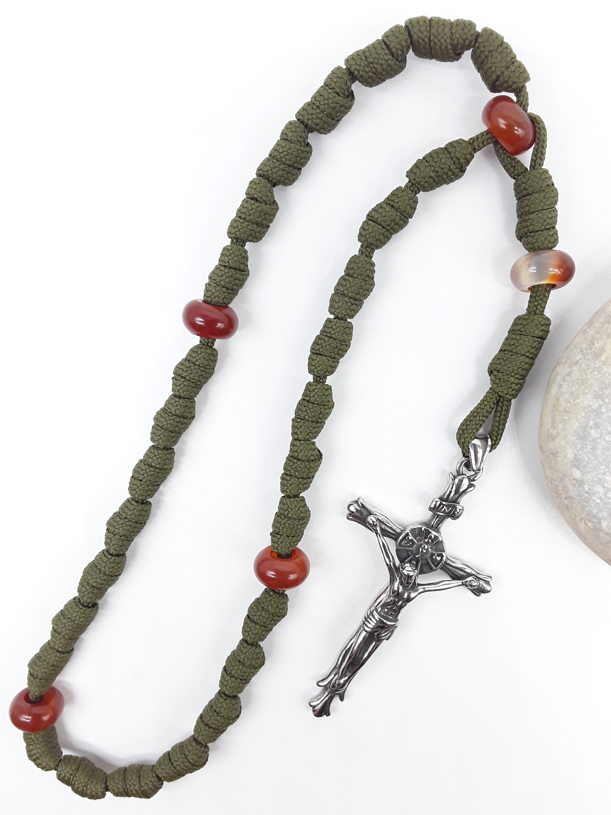 The Quiet Sentinel Paracord Anglican Prayer Beads by Polmadeva beside natural stone, featuring Carnelian and stainless steel crucifix