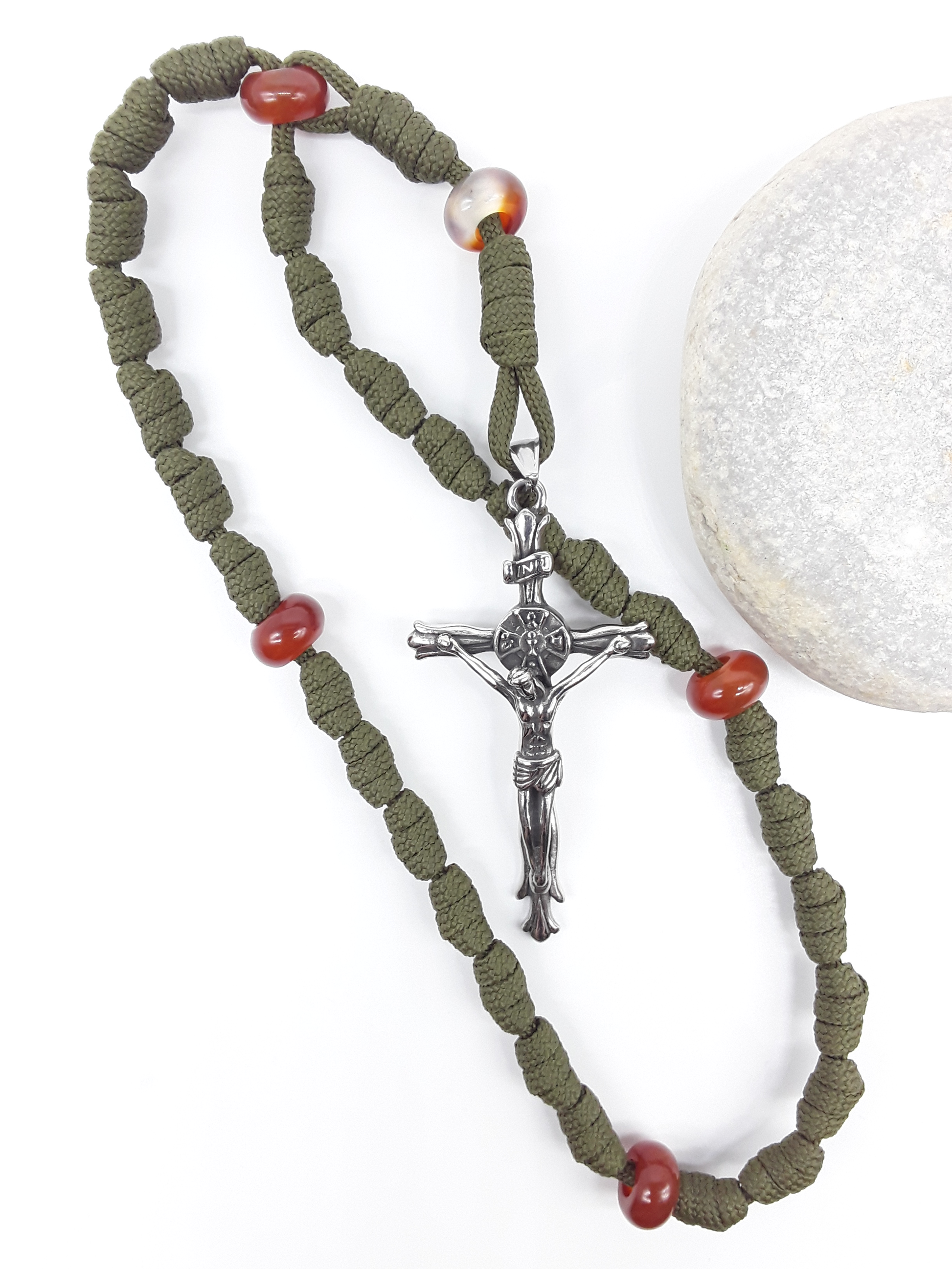 The Quiet Sentinel Paracord Anglican Prayer Beads by Polmadeva beside natural stone, featuring Carnelian and stainless steel crucifix