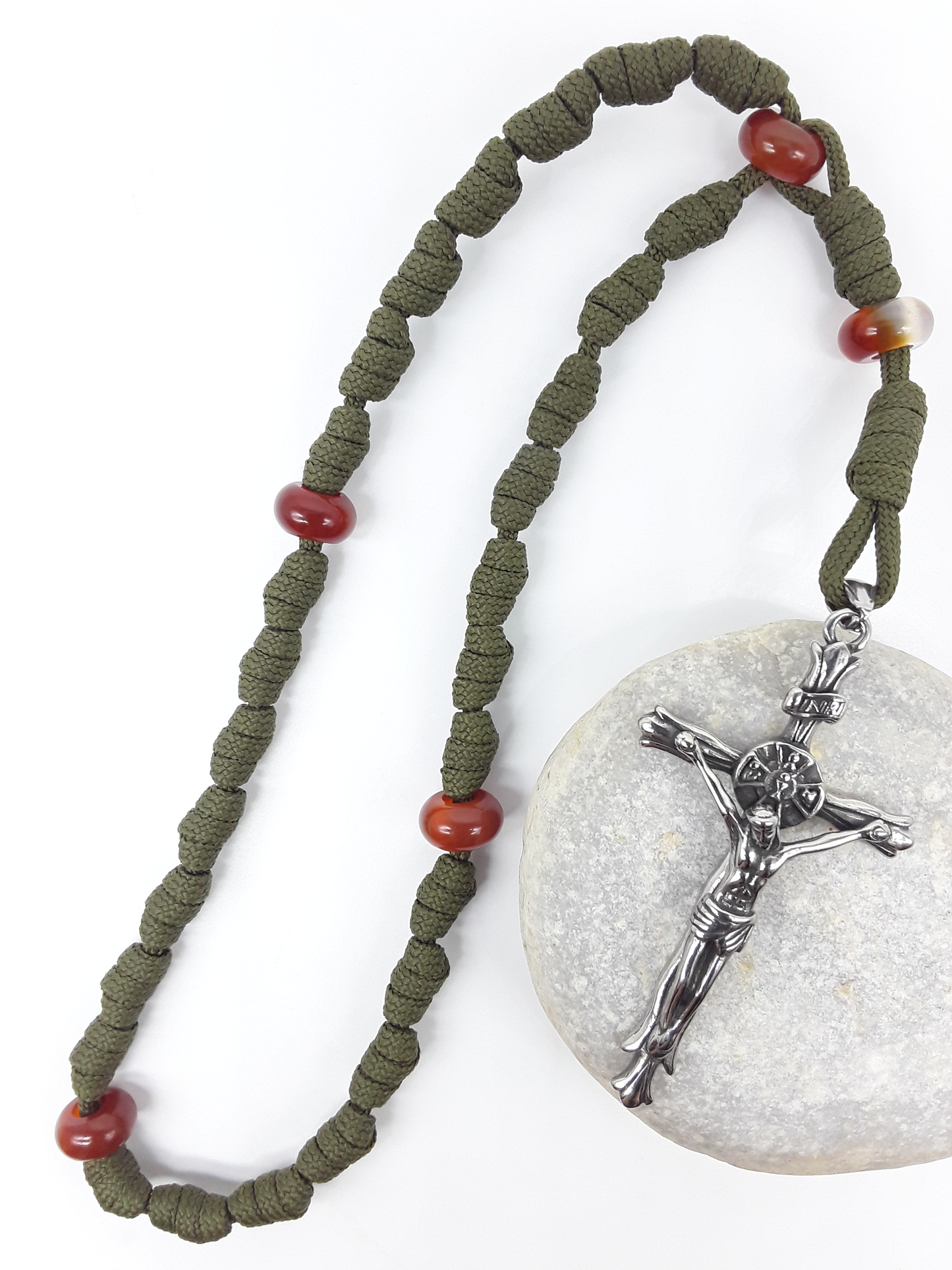 The Quiet Sentinel Paracord Anglican Prayer Beads by Polmadeva placed on stone, crafted with Carnelian and antique silver crucifix