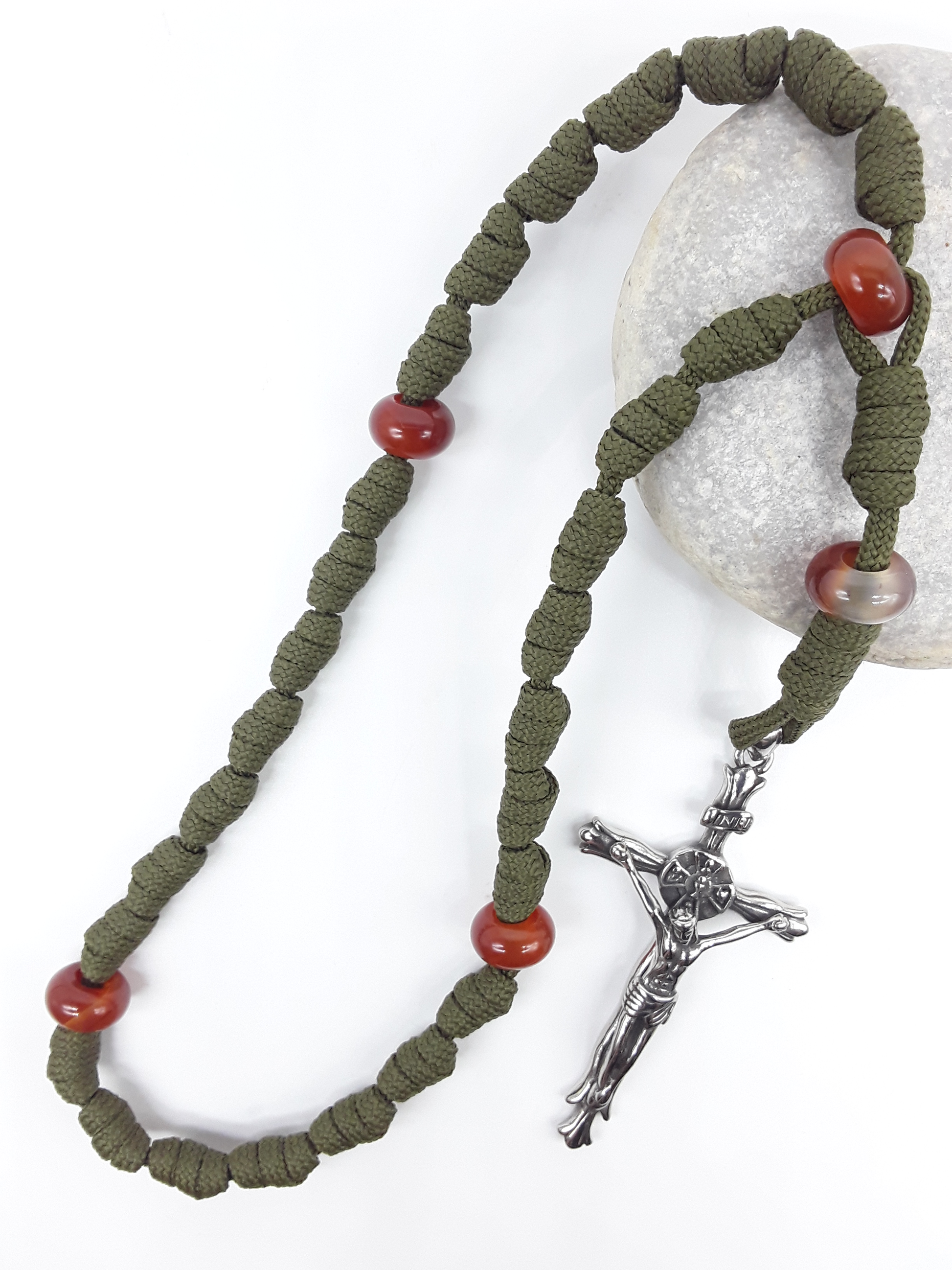 The Quiet Sentinel Paracord Anglican Prayer Beads by Polmadeva placed on stone, crafted with Carnelian and antique silver crucifix