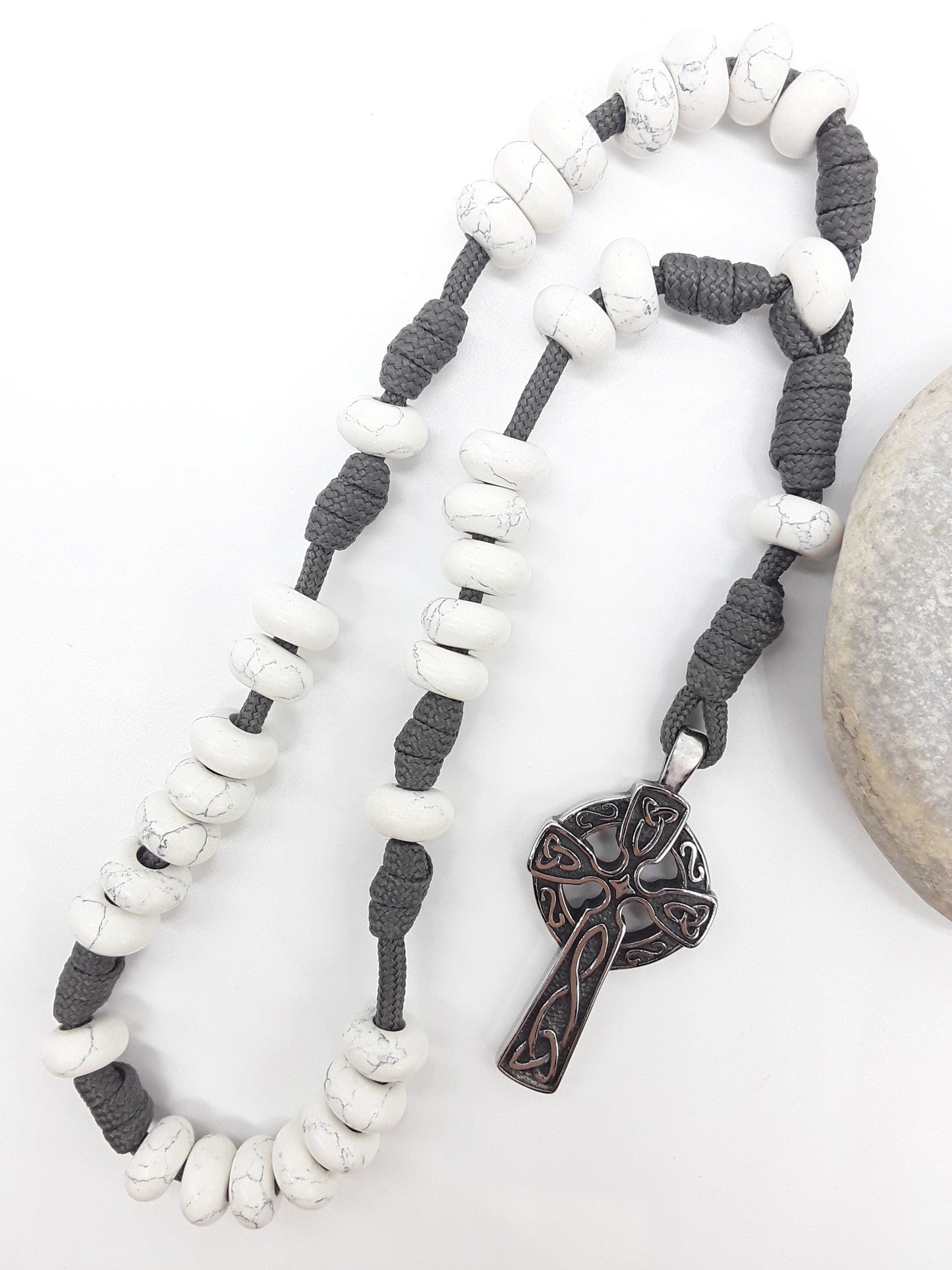 The Quiet Structure Paracord Anglican Prayer Beads by Polmadeva beside natural stone, featuring Howlite and Celtic cross