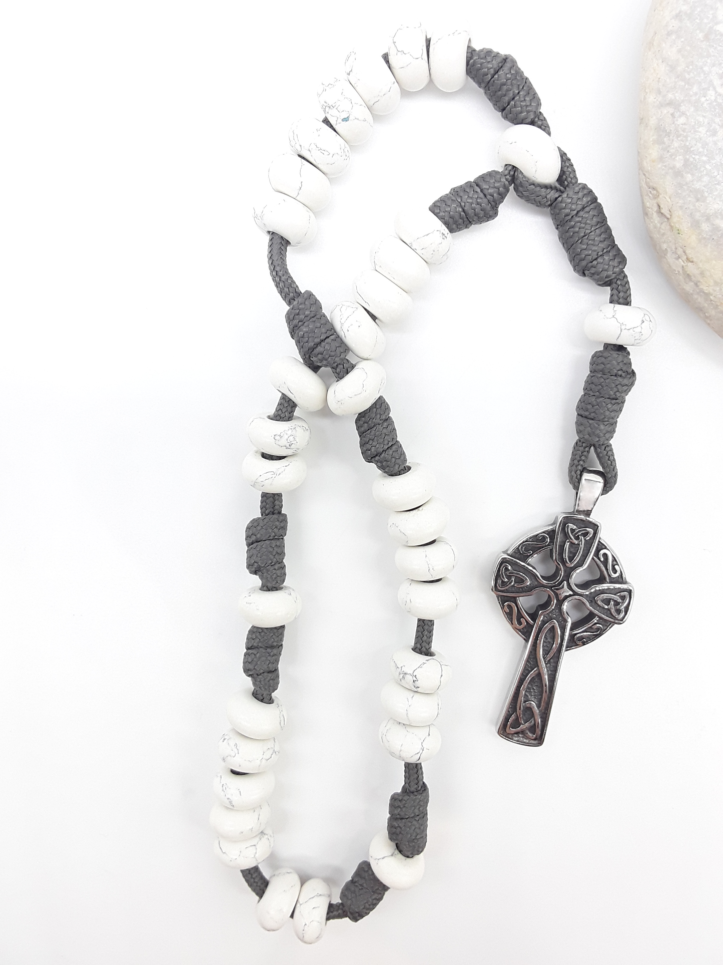 The Quiet Structure Paracord Anglican Prayer Beads by Polmadeva beside natural stone, featuring Howlite and Celtic cross
