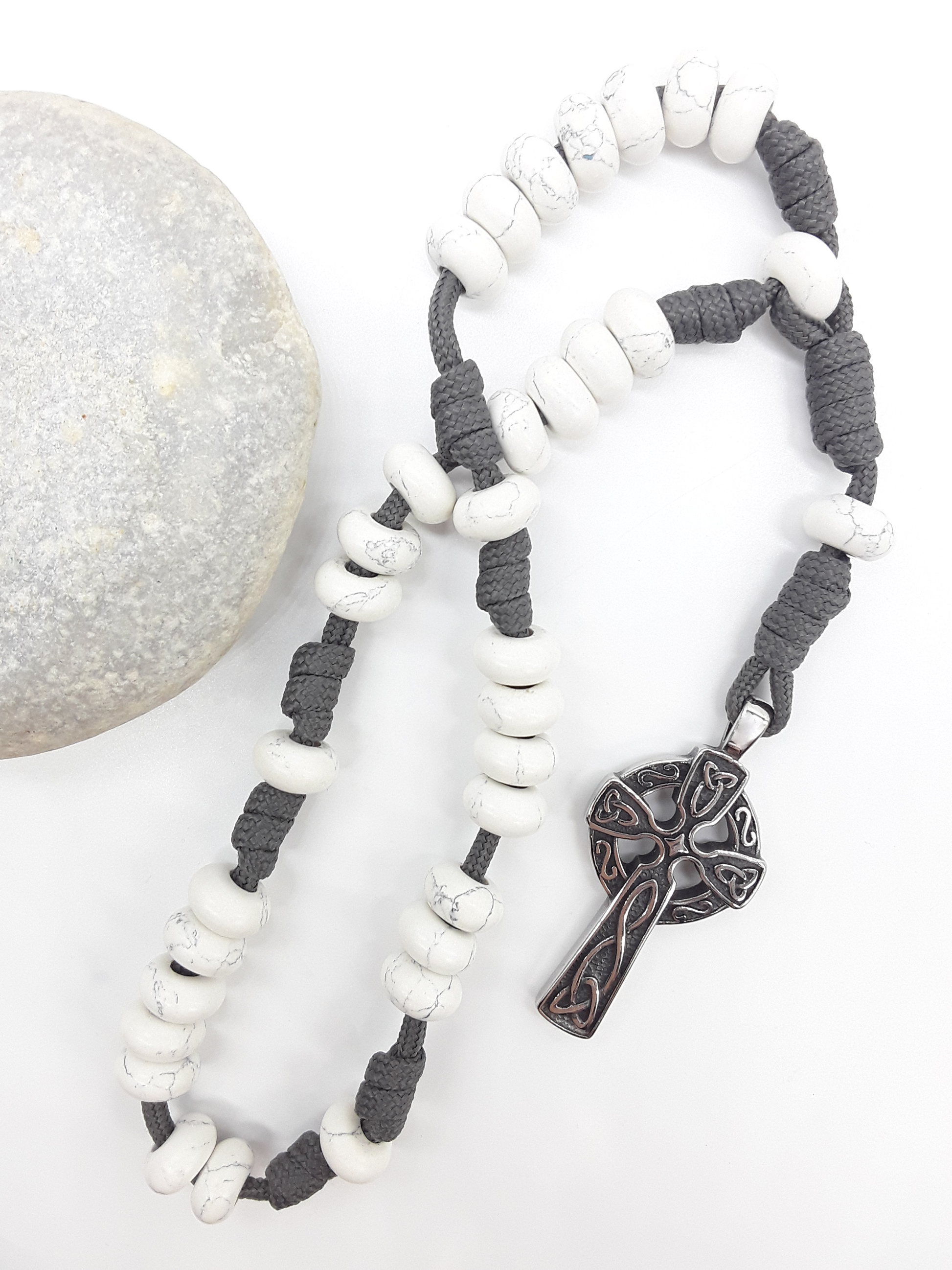 The Quiet Structure Paracord Anglican Prayer Beads by Polmadeva beside natural stone, featuring Howlite and Celtic cross