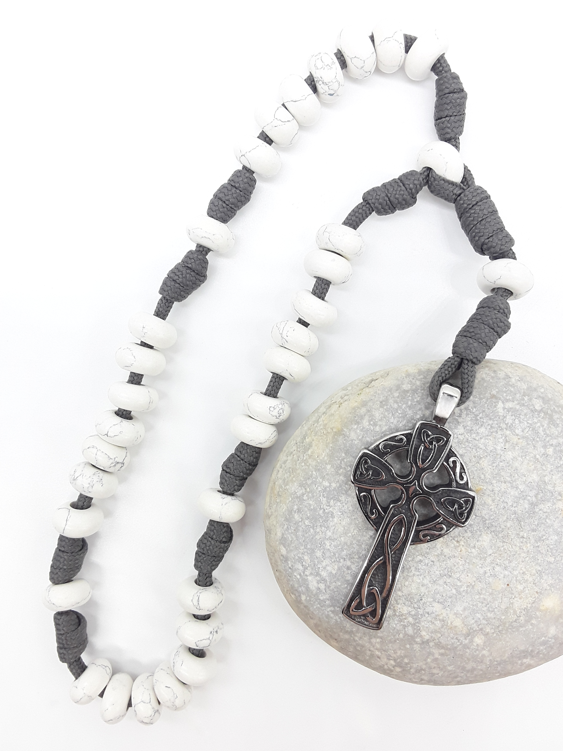 The Quiet Structure Paracord Anglican Prayer Beads by Polmadeva placed on stone, crafted with Howlite and stainless steel Celtic cross