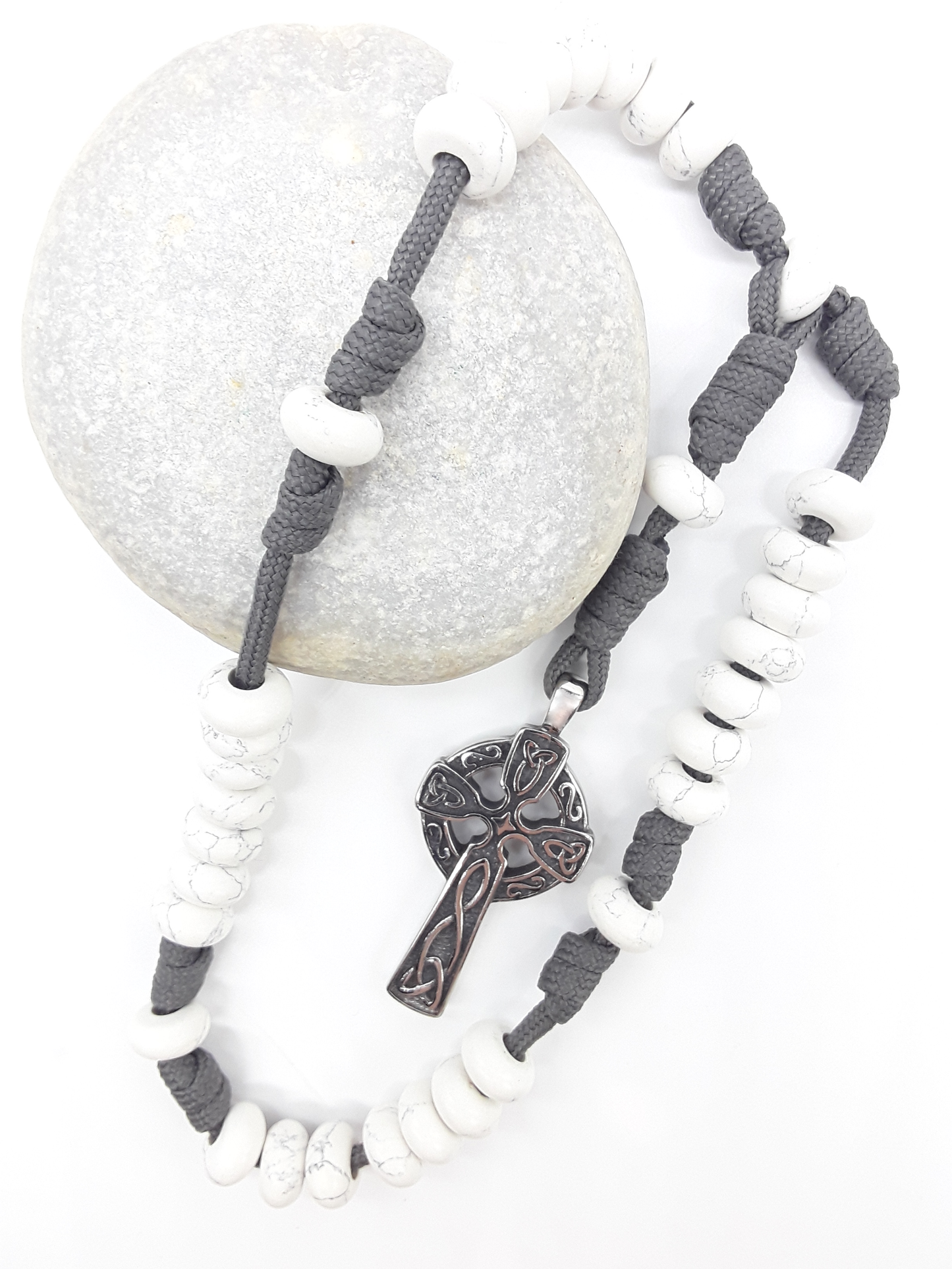 The Quiet Structure Paracord Anglican Prayer Beads by Polmadeva placed on stone, crafted with Howlite and stainless steel Celtic cross