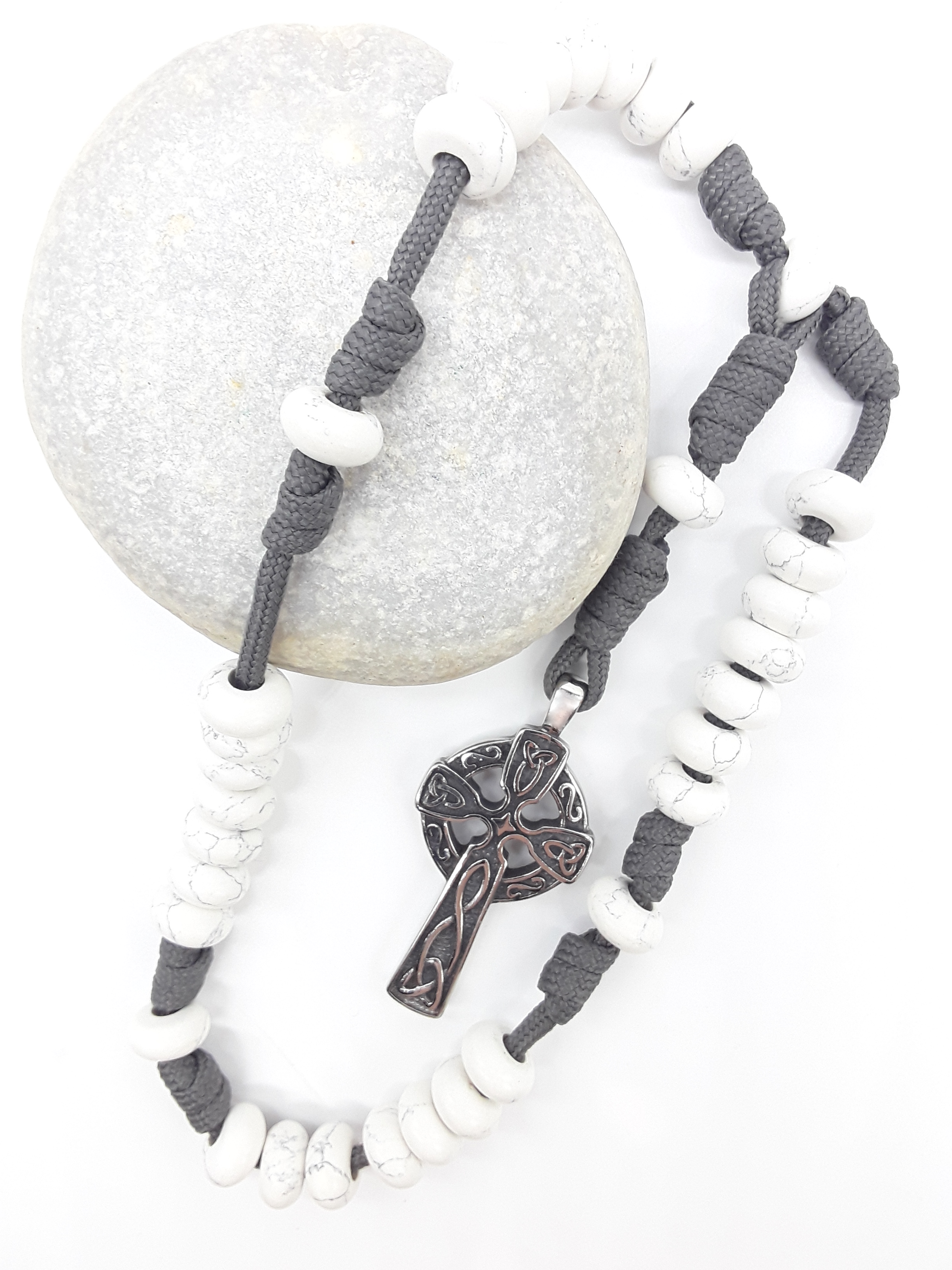 The Quiet Structure Paracord Anglican Prayer Beads by Polmadeva placed on stone, crafted with Howlite and stainless steel Celtic cross