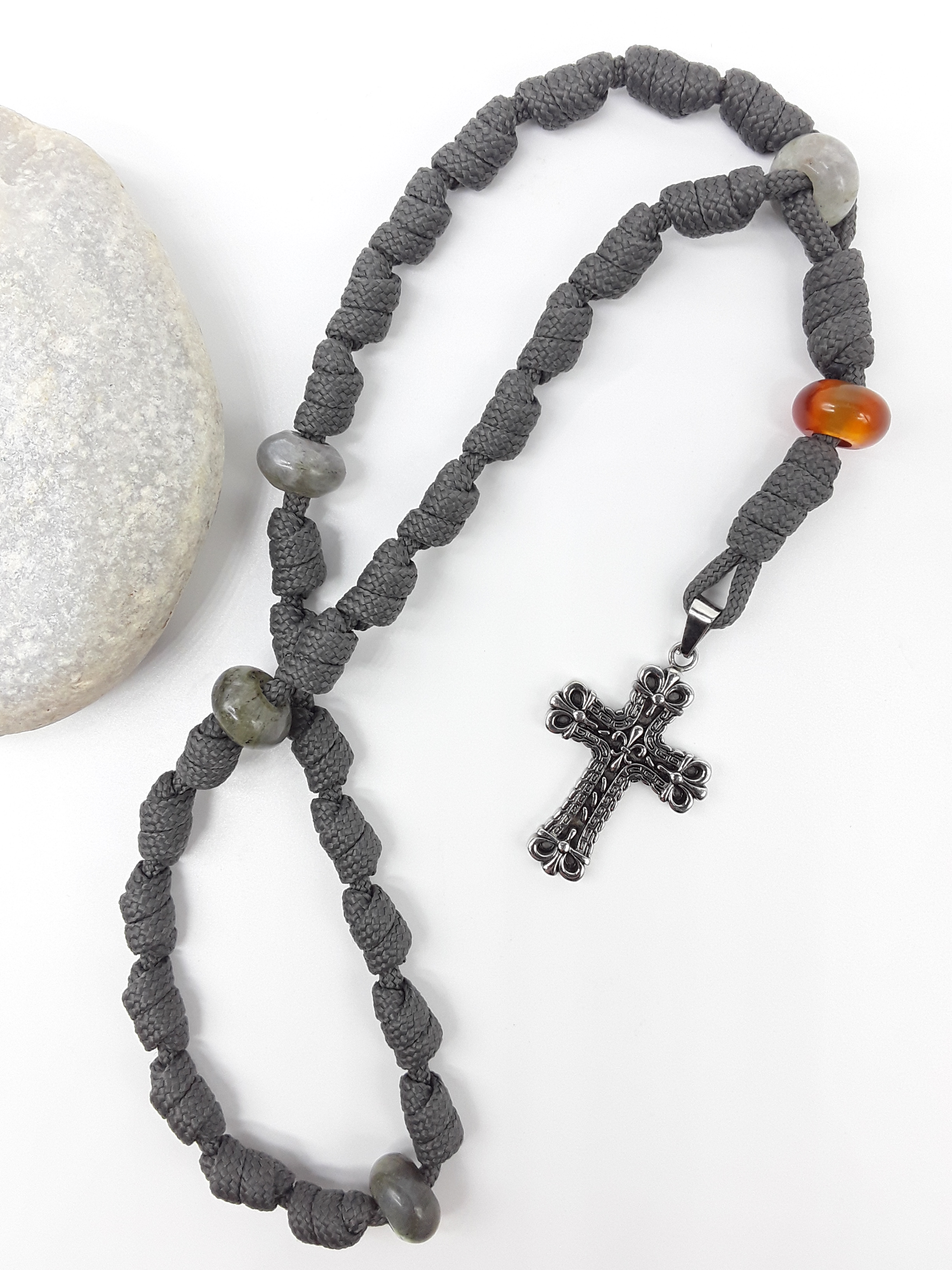 The Quiet Way Antique Floral Anglican Rosary by Polmadeva with hand-knotted cord, Carnelian and Labradorite elements, and floral stainless steel cross beside stone.