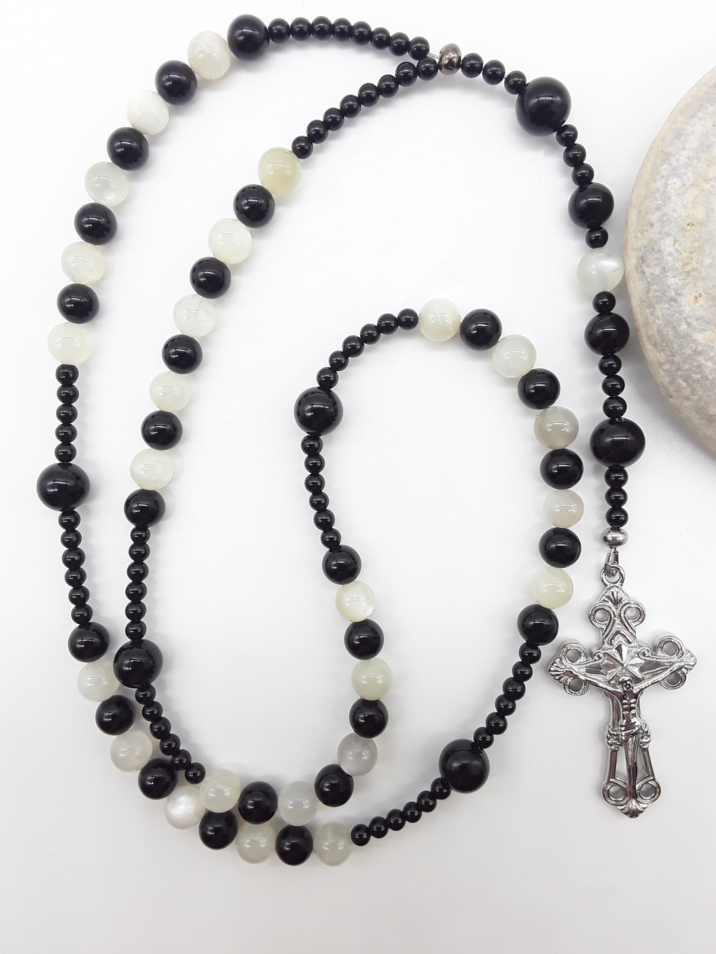 Black Onyx and Moonstone Catholic rosary with a crucifix, photographed alongside a natural stone on a white surface.