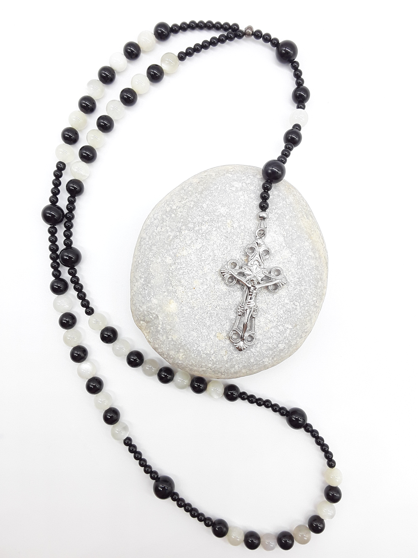Black Onyx and Moonstone Catholic rosary with a crucifix, photographed over a natural stone on a white surface.