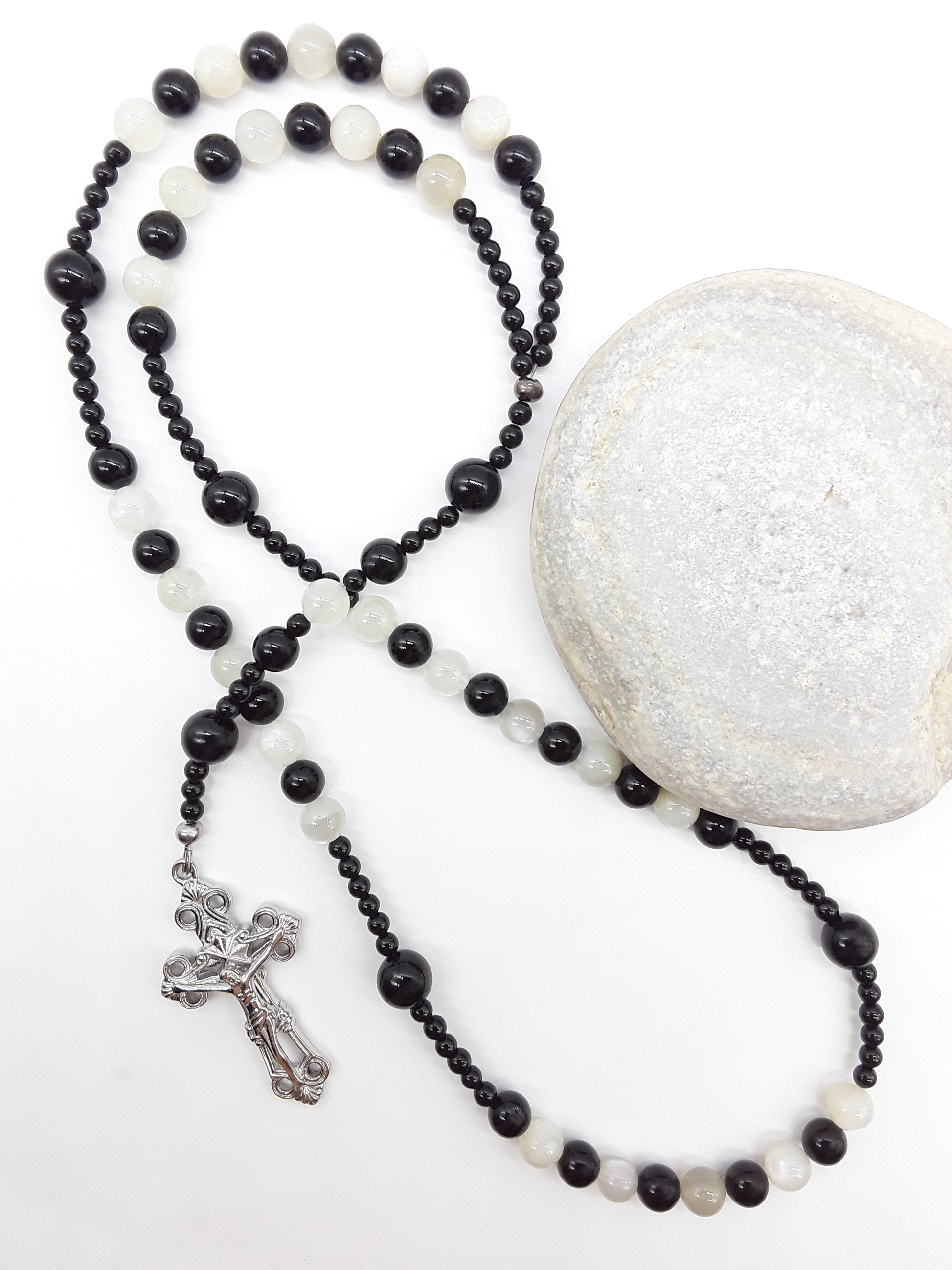 Black Onyx and Moonstone Catholic rosary with a crucifix, photographed alongside a natural stone on a white surface.