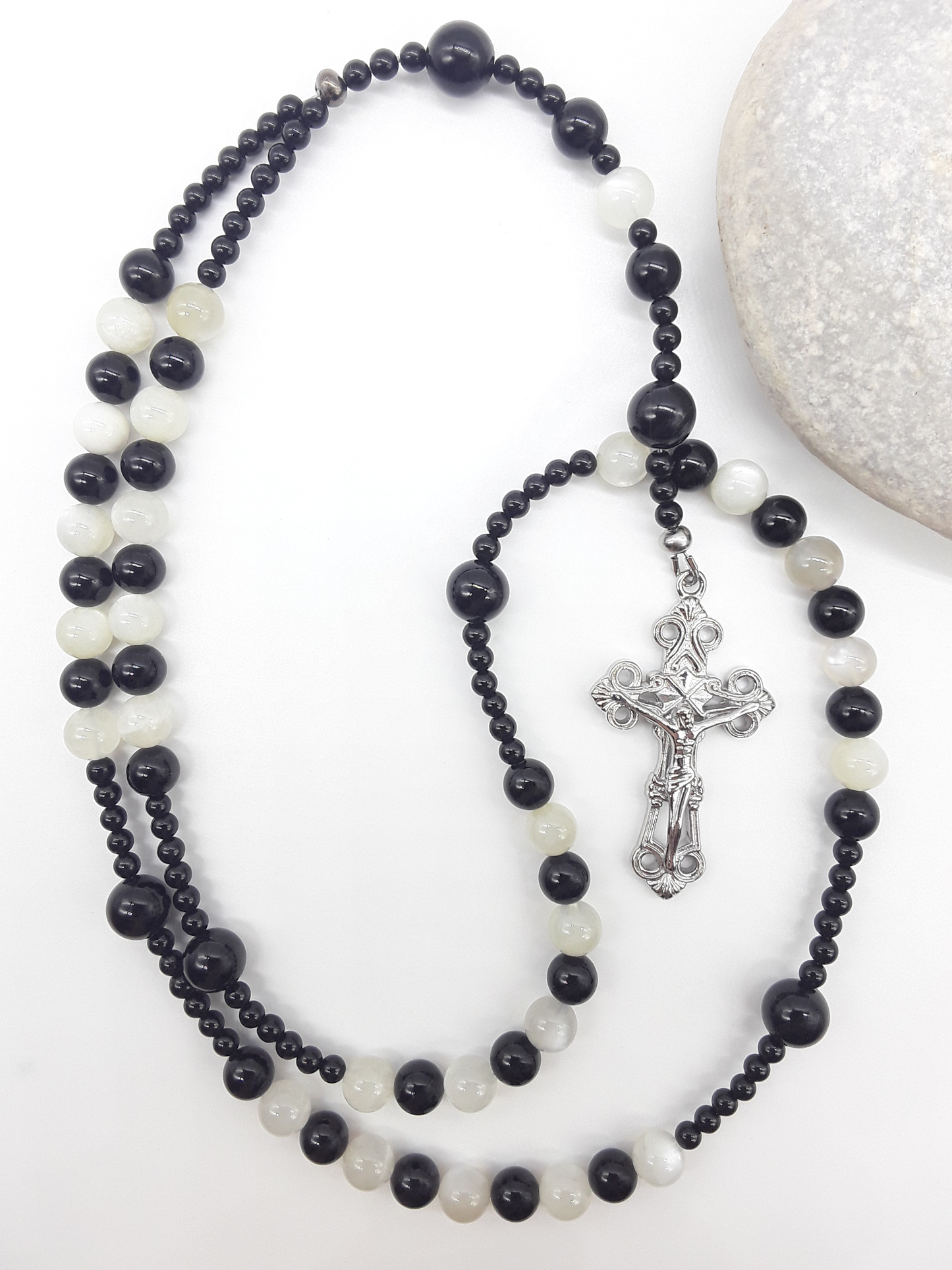 Black Onyx and Moonstone Catholic rosary with a crucifix, photographed alongside a natural stone on a white surface.