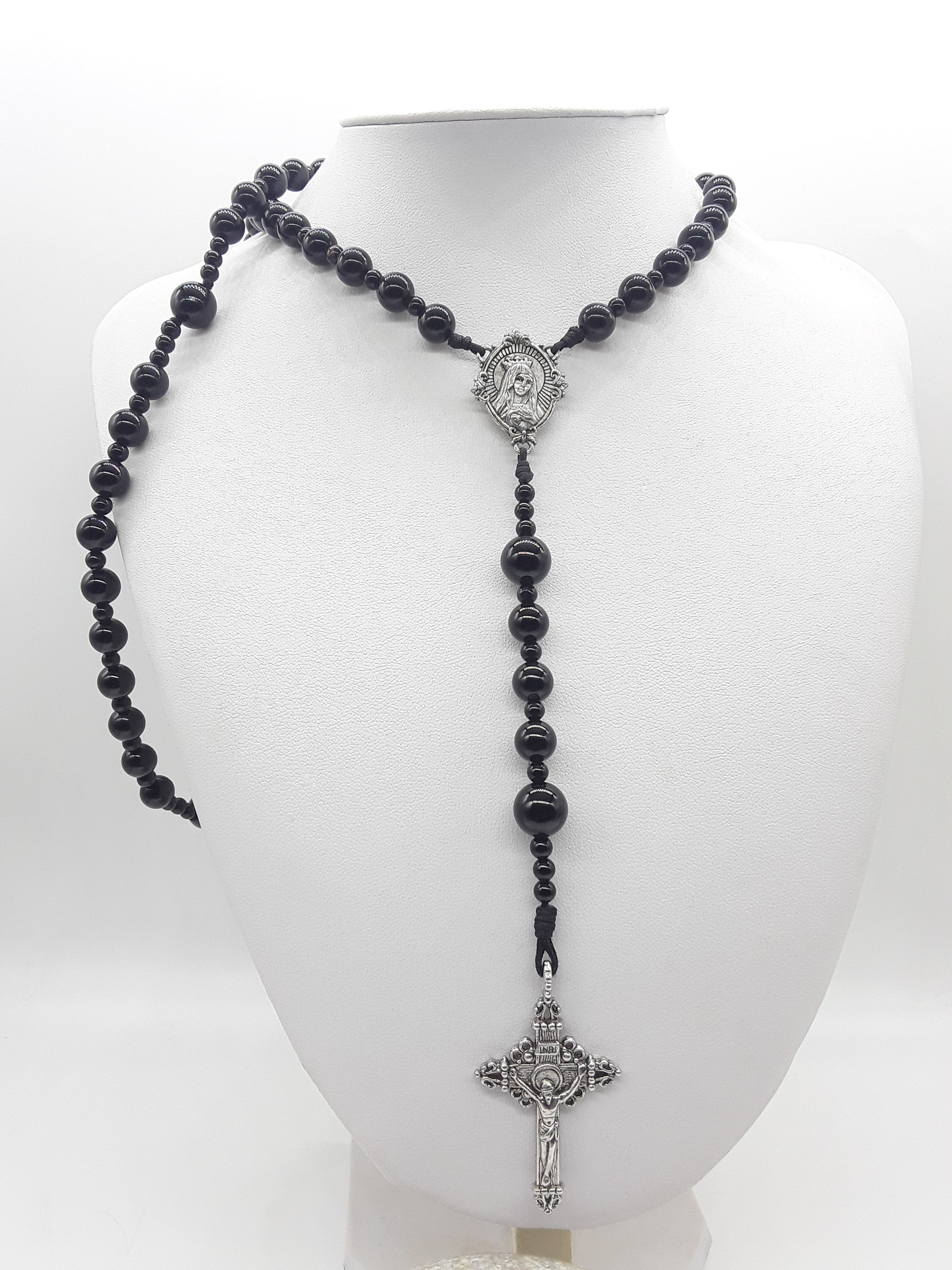 Traditional Catholic rosary with black onyx beads, tin Virgin Mary centerpiece, and tin crucifix displayed on a white mannequin bust.