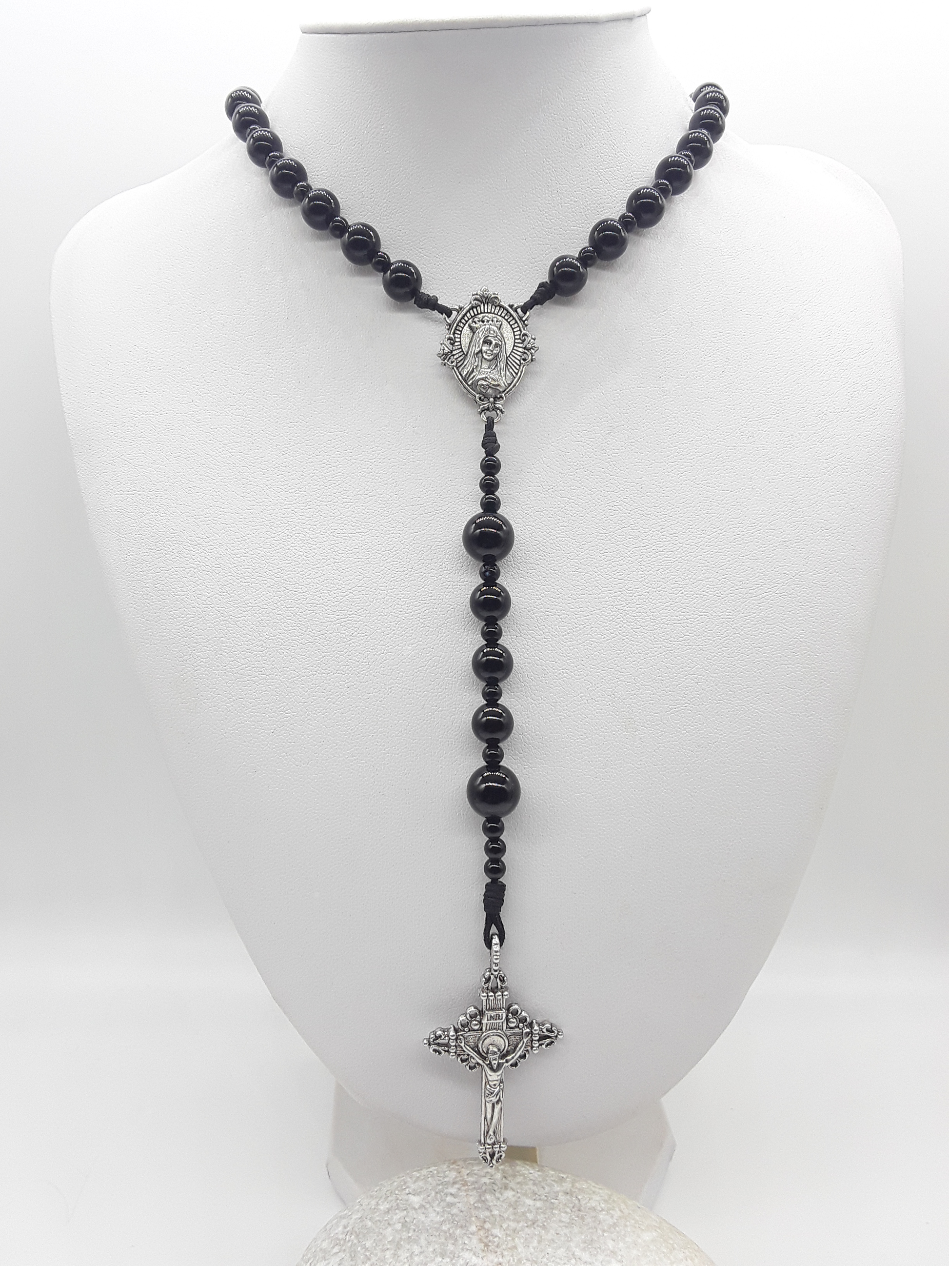 Traditional Catholic rosary with black onyx beads, tin Virgin Mary centerpiece, and tin crucifix displayed on a white mannequin bust.