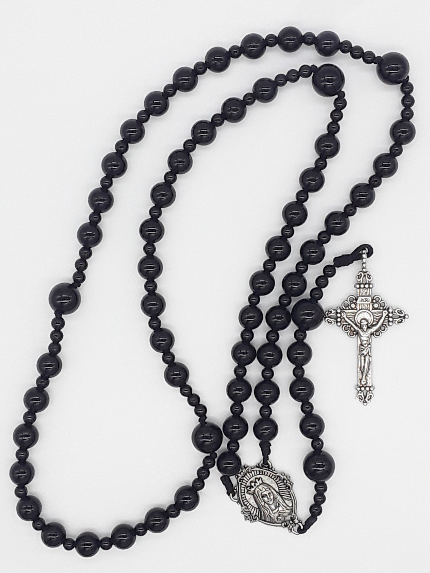 Black onyx Catholic rosary featuring a tin Virgin Mary medallion and traditional tin crucifix, arranged on a light neutral background.