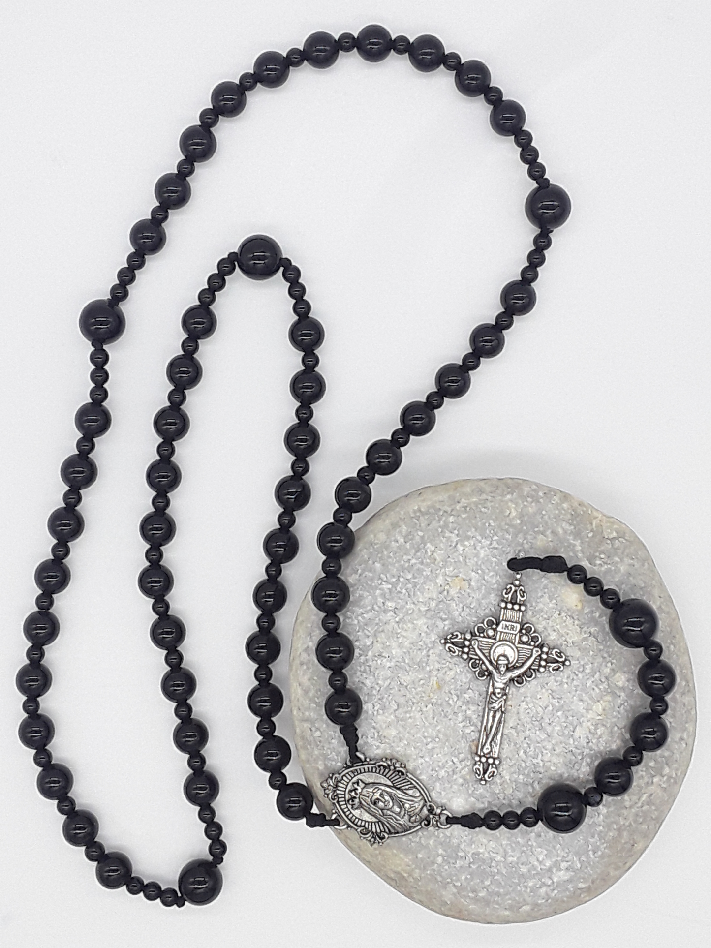 Black onyx Catholic rosary featuring a tin Virgin Mary medallion and traditional tin crucifix, arranged on a light neutral background.