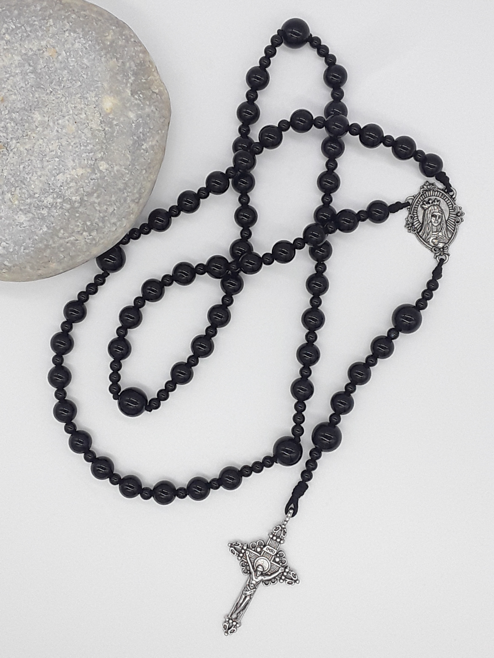 Black onyx Catholic rosary featuring a tin Virgin Mary medallion and traditional tin crucifix, arranged on a light neutral background.