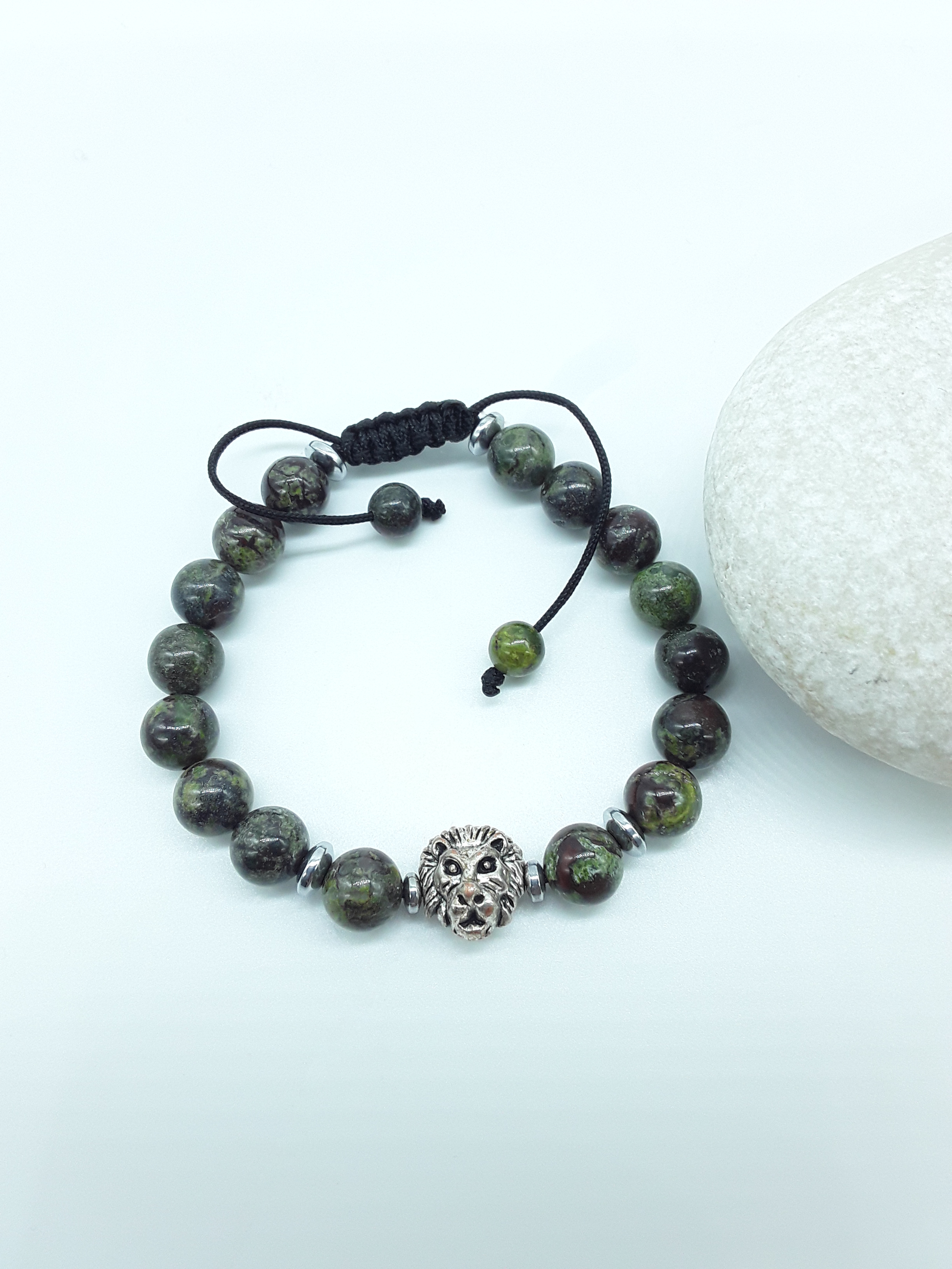 Handcrafted dragon blood stone beaded bracelet with a metal lion element, displayed on a natural stone surface