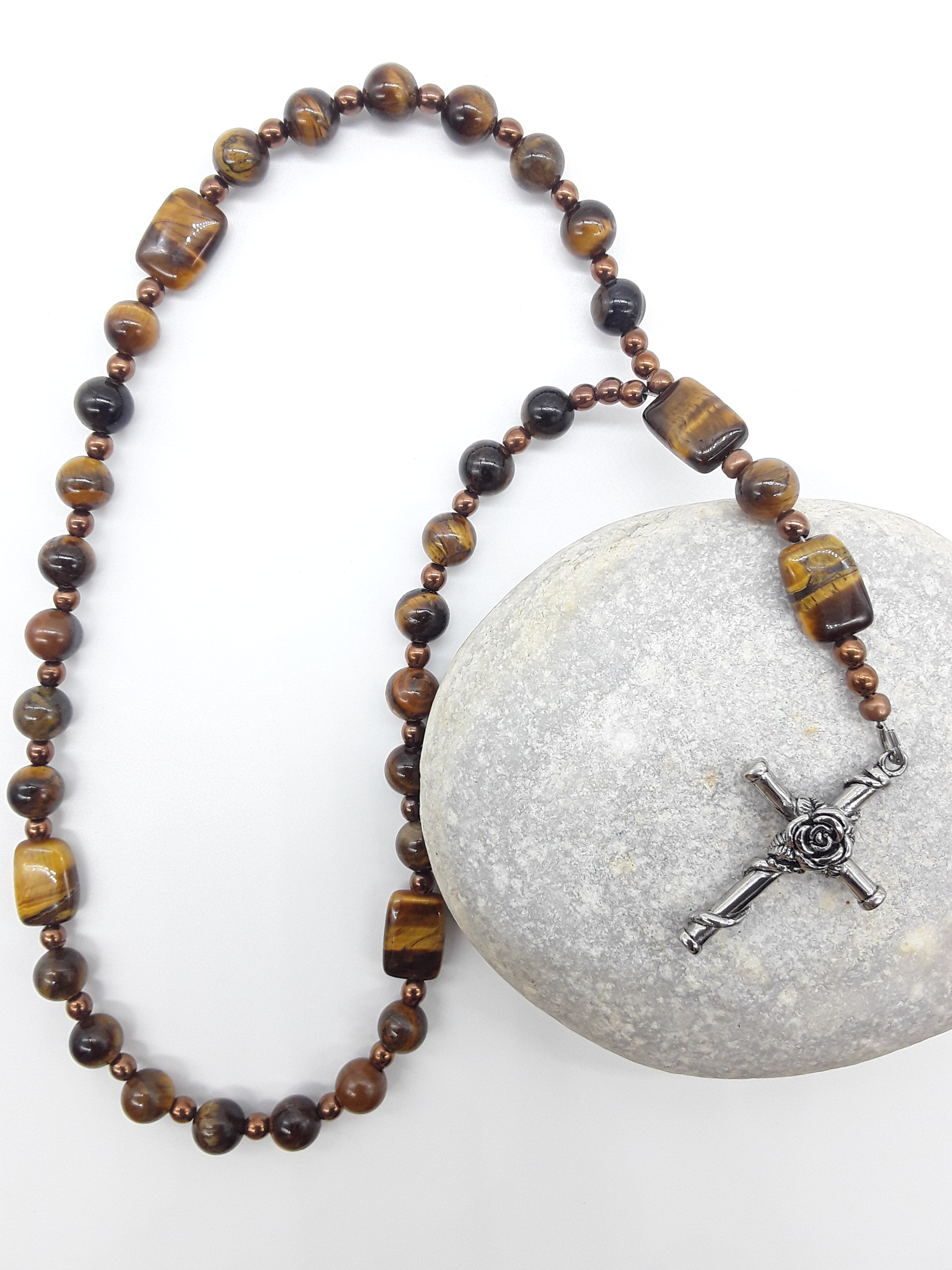 The Steady Gaze Anglican Prayer Beads by Polmadeva placed on stone, crafted with Tiger’s Eye, Hematite, and Rosicrucian Cross