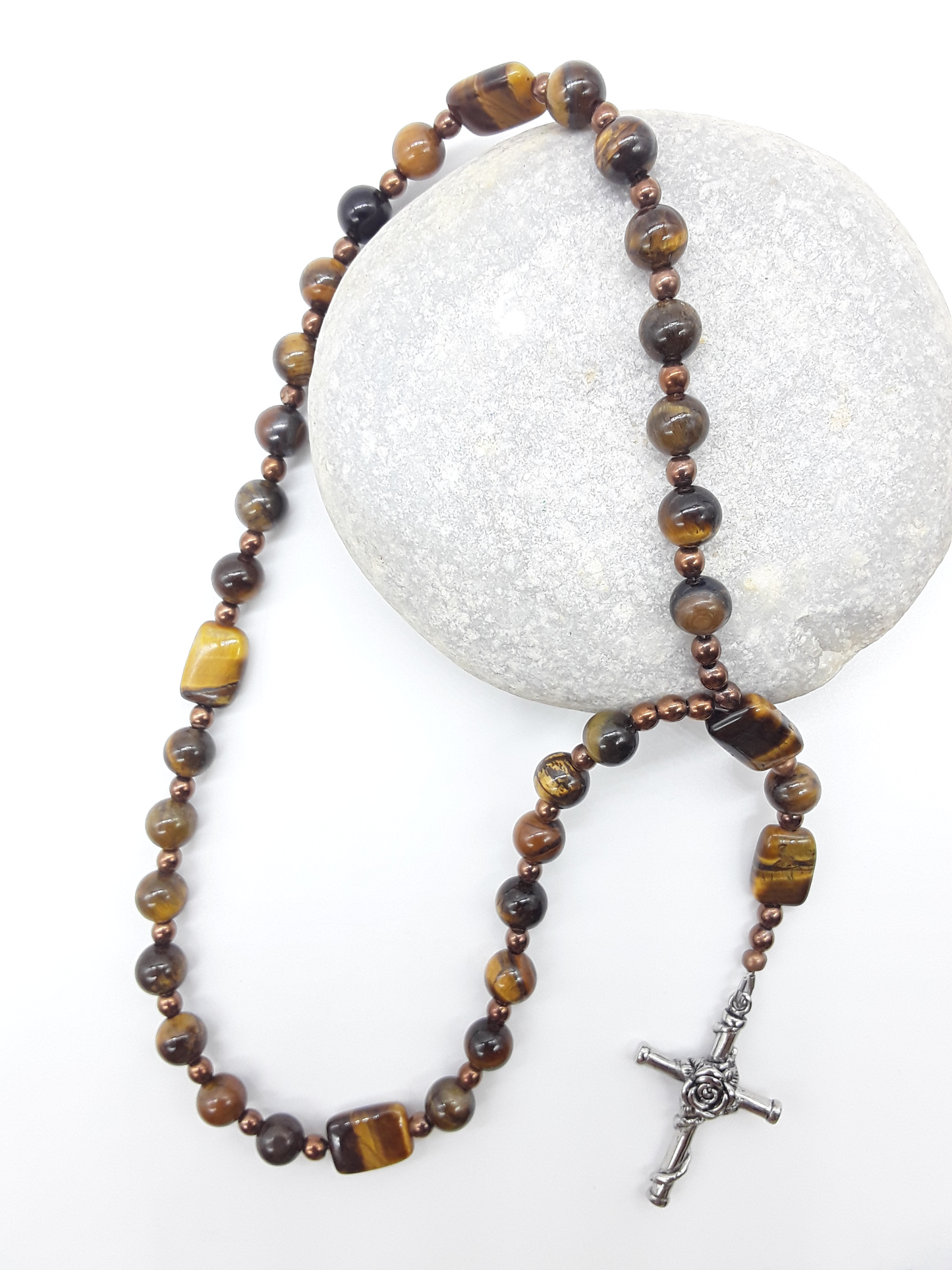 The Steady Gaze Anglican Prayer Beads by Polmadeva placed on stone, crafted with Tiger’s Eye, Hematite, and Rosicrucian Cross