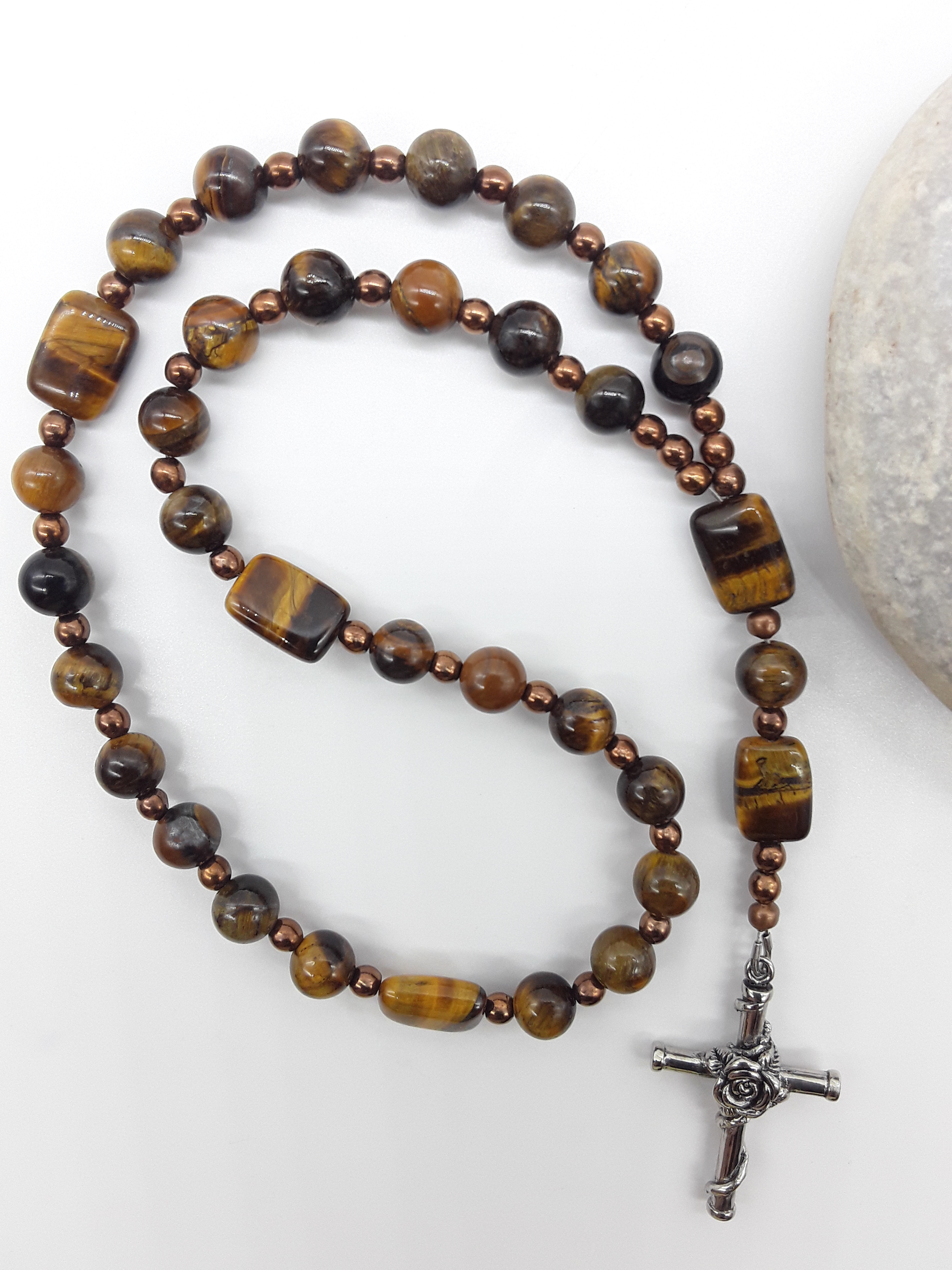 The Steady Gaze Anglican Prayer Beads by Polmadeva beside natural stone, featuring Tiger’s Eye, Hematite, and Rosicrucian Cross