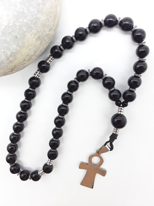 The Steady Presence — Black Onyx Orthodox Rosary by Polmadeva, black onyx beads with hematite spacers and stainless steel cross, photographed beside natural stone to emphasize grounded prayer and steady presence.