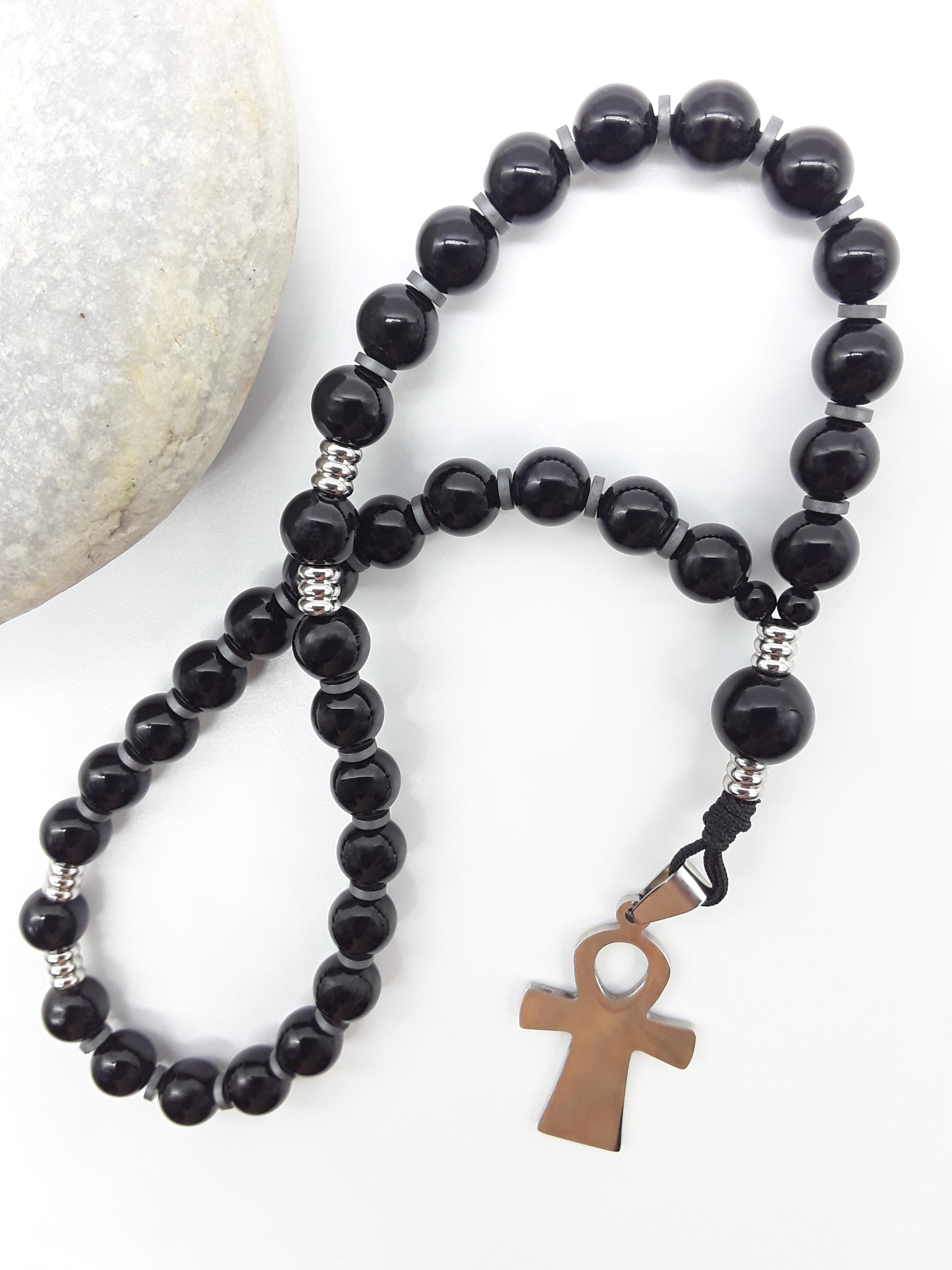 The Steady Presence — Black Onyx Orthodox Rosary by Polmadeva, black onyx beads with hematite spacers and stainless steel cross, photographed beside natural stone to emphasize grounded prayer and steady presence.