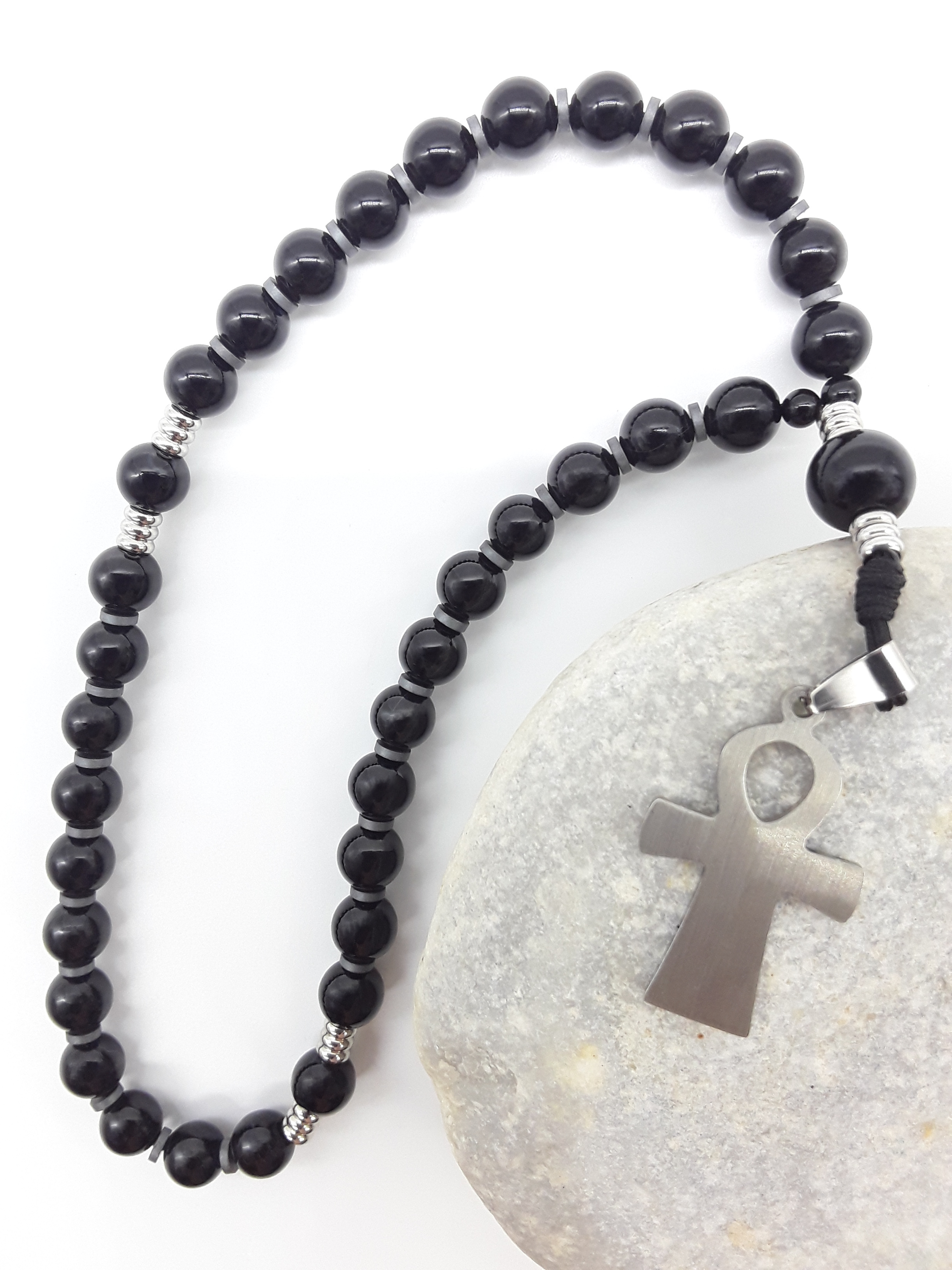 The Steady Presence — Black Onyx Orthodox Rosary by Polmadeva, black onyx beads and stainless steel cross resting on natural stone, highlighting weight, continuity, and quiet repetition.