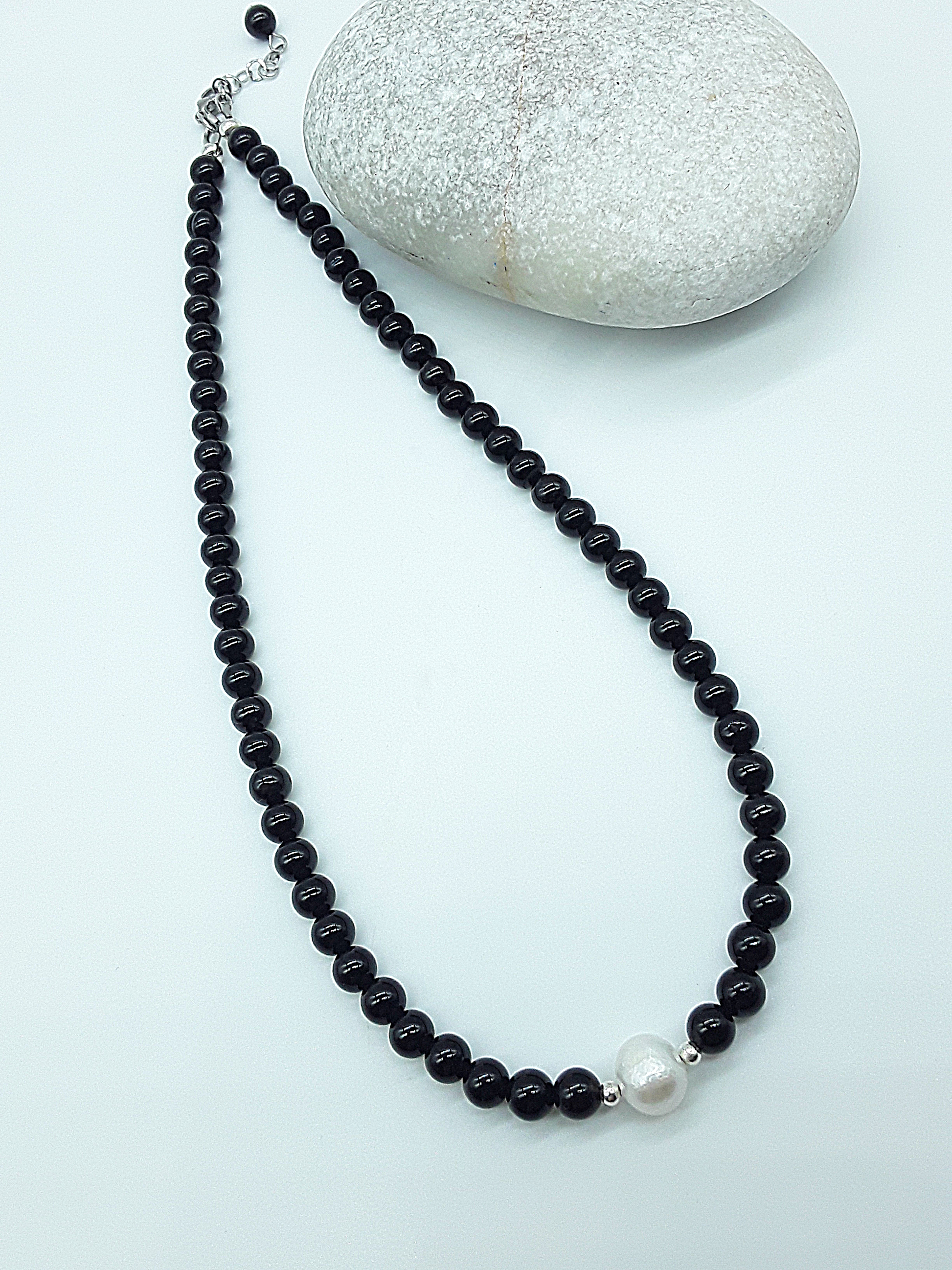 Still Core Necklace by Polmadeva with black onyx beads and single pearl shown in full length beside natural stone