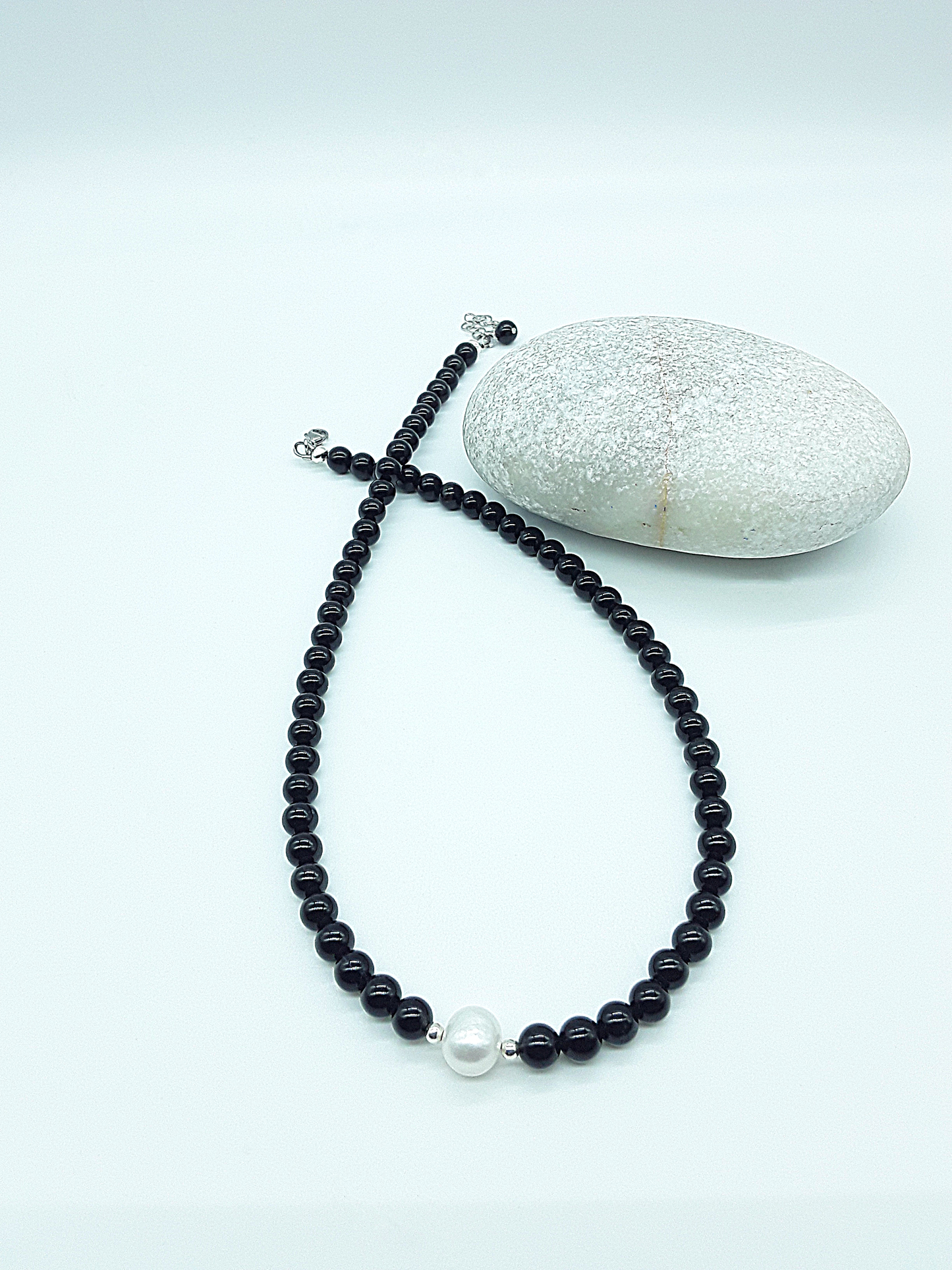 Still Core Necklace by Polmadeva with black onyx beads and single pearl arranged in crossed composition beside natural stone