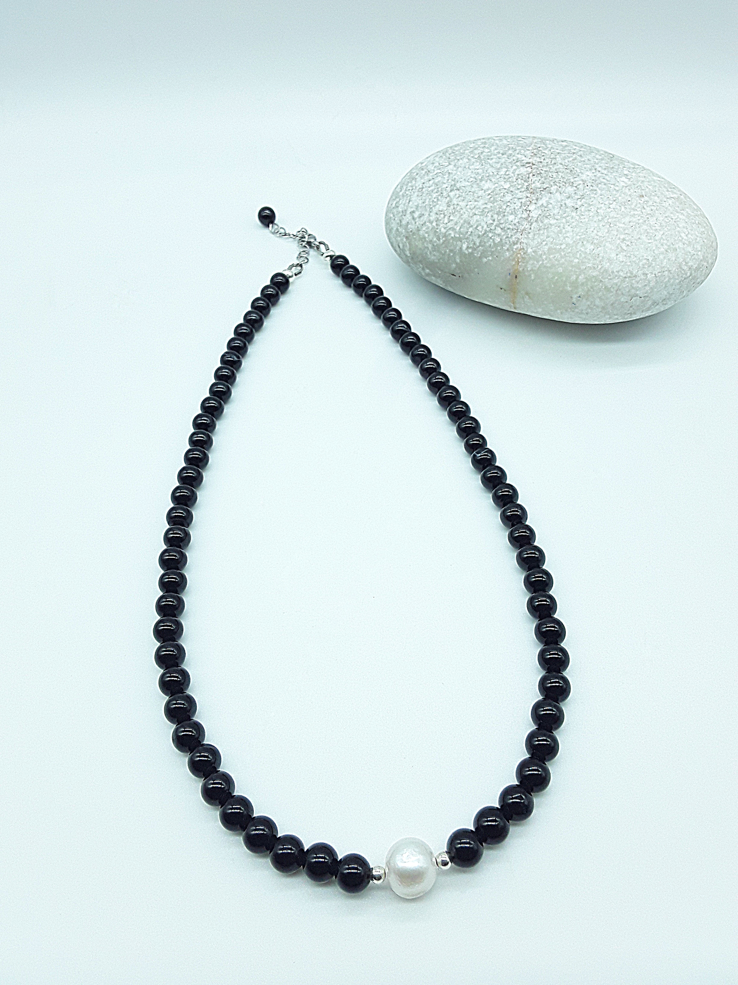 Still Core Necklace by Polmadeva with black onyx beads and single pearl shown in full length beside natural stone, Sacred Balance collection