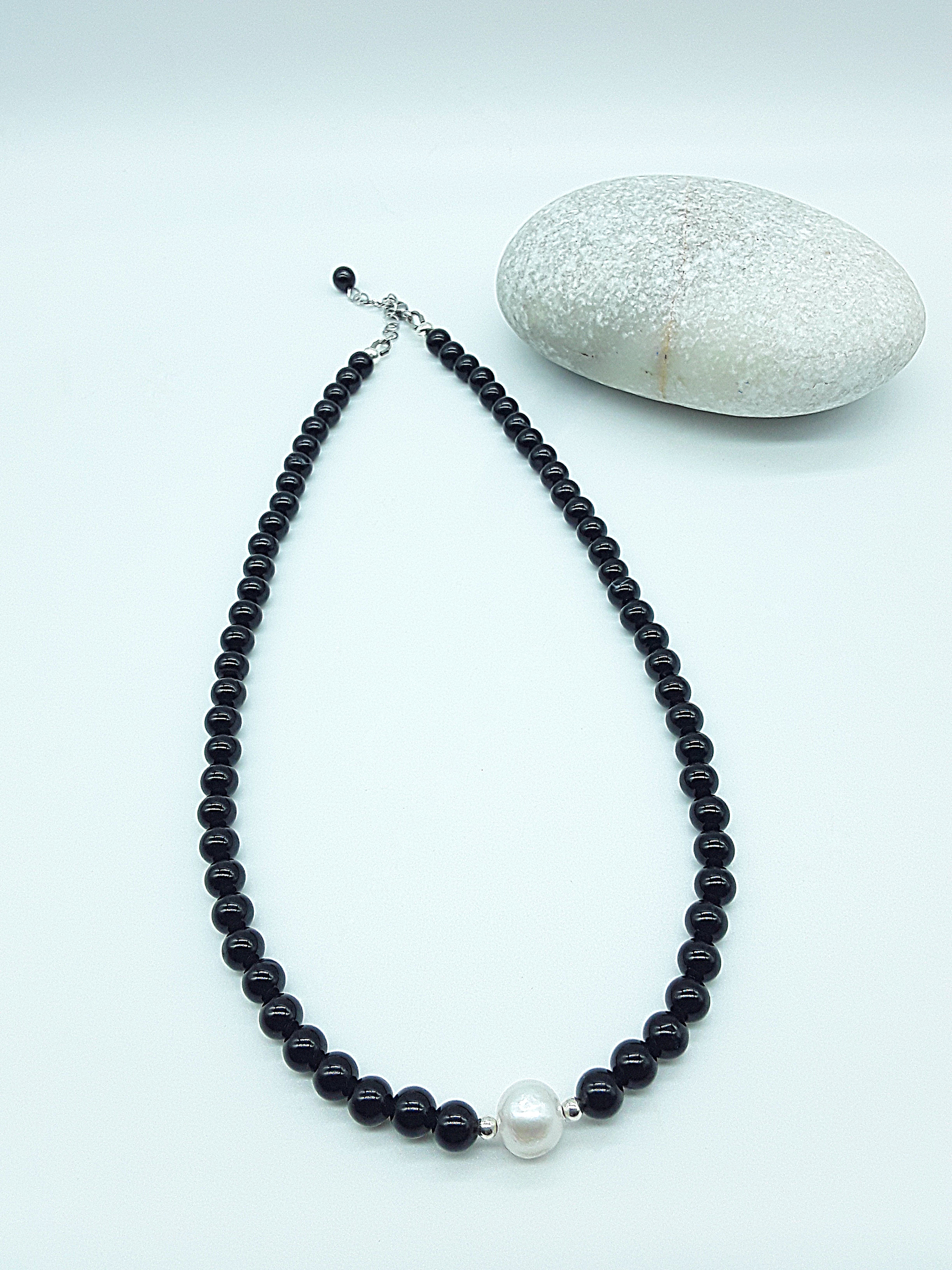 Still Core Necklace by Polmadeva with black onyx beads and single pearl shown in full length beside natural stone, Sacred Balance collection