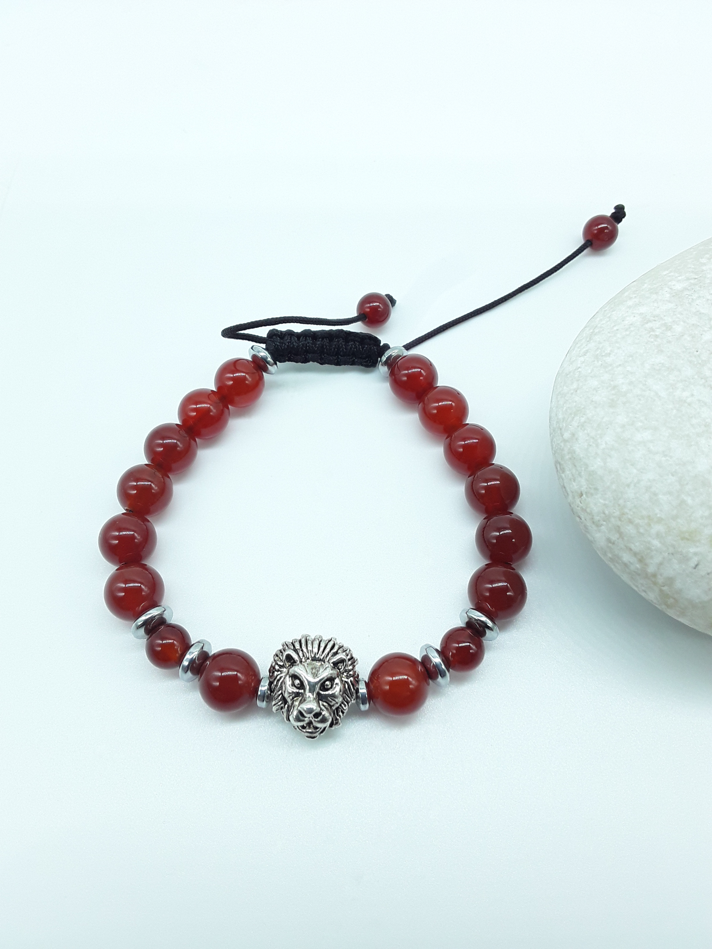 Carnelian and Hematite bracelet with lion element resting on natural stone, minimal editorial style