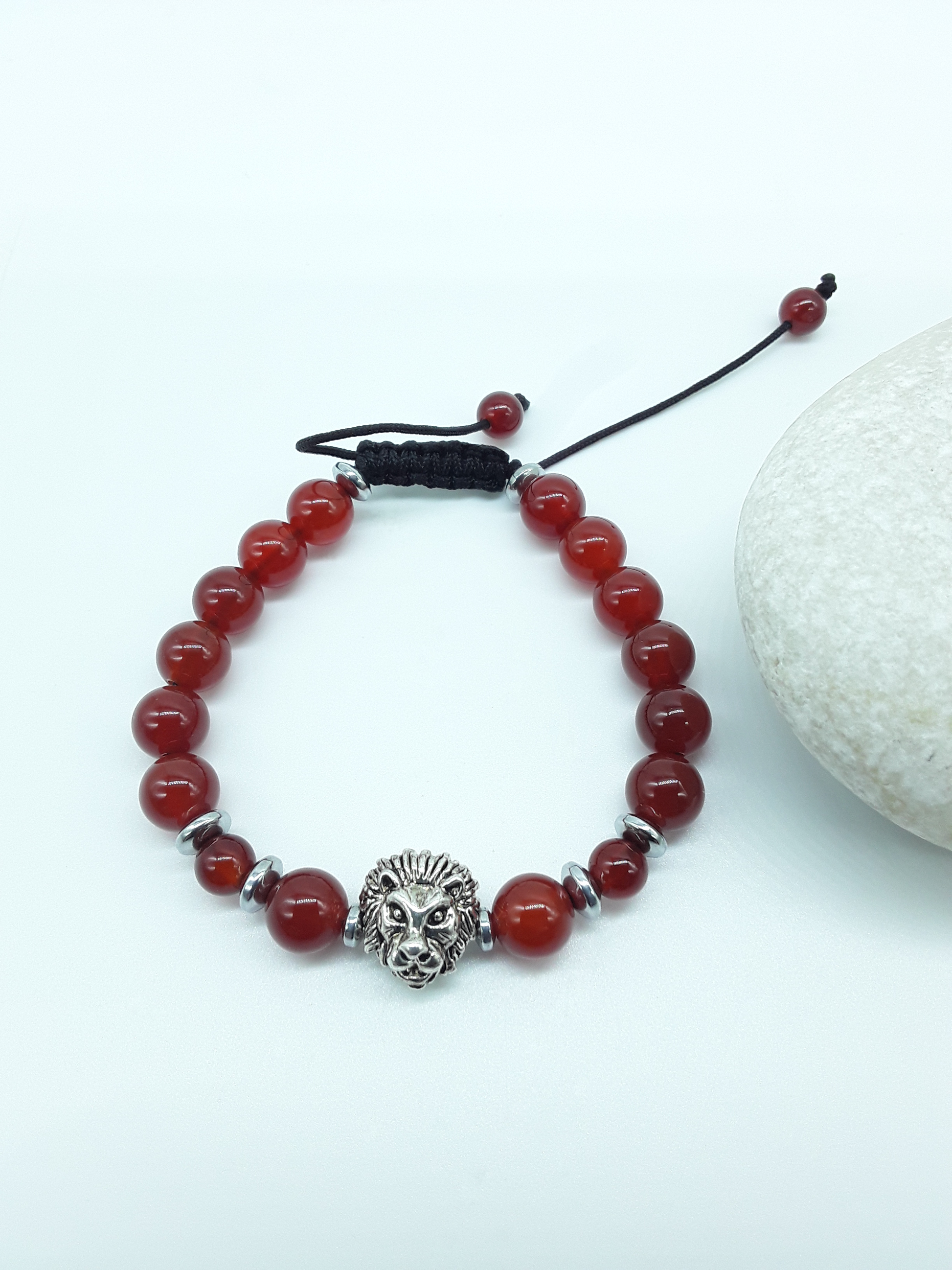 Carnelian and Hematite bracelet with lion element resting on natural stone, minimal editorial style