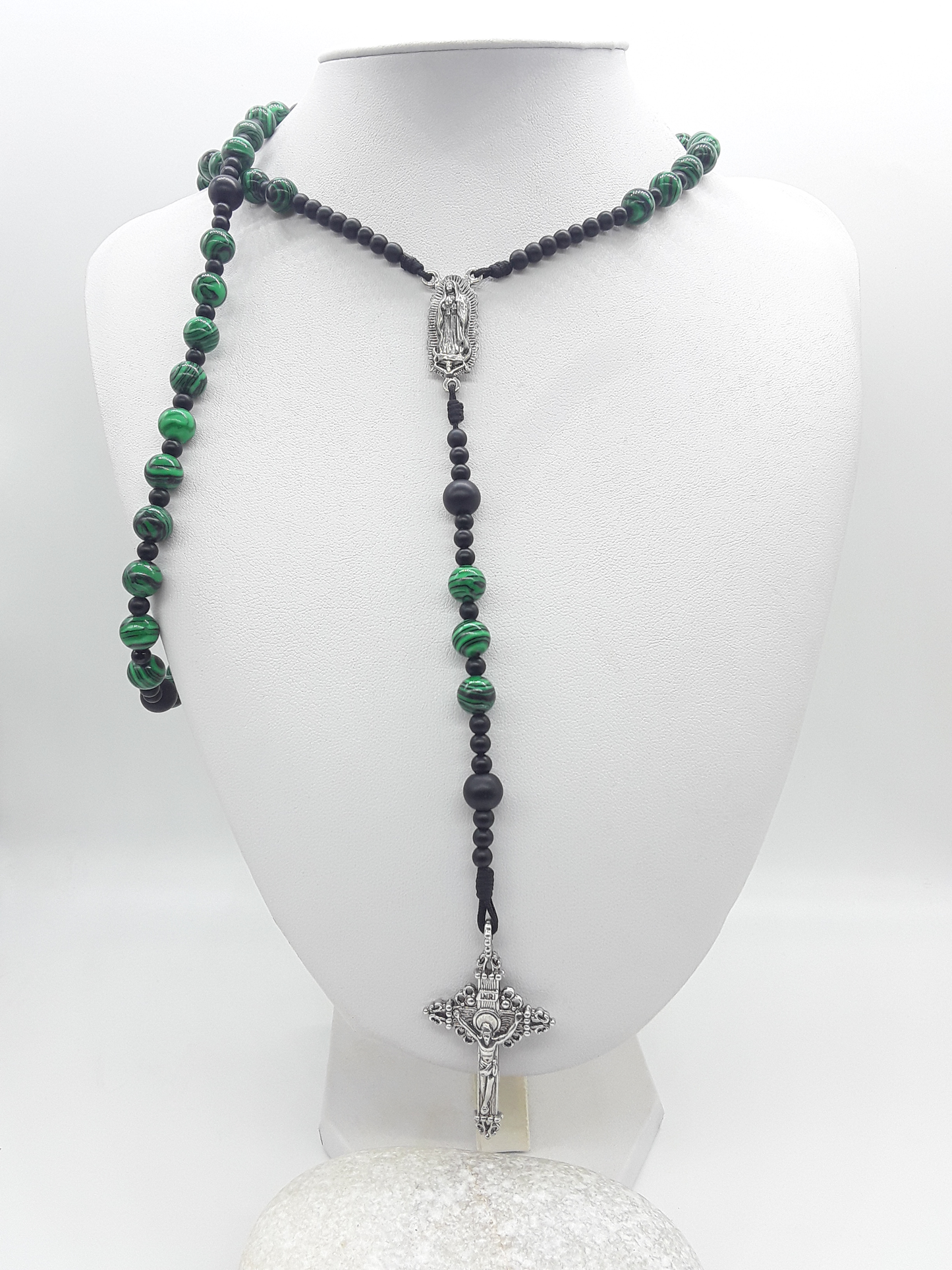 Catholic rosary with black onyx and malachite beads, featuring Our Lady of Guadalupe medallion and a silver-toned crucifix, displayed on a mannequin bust.