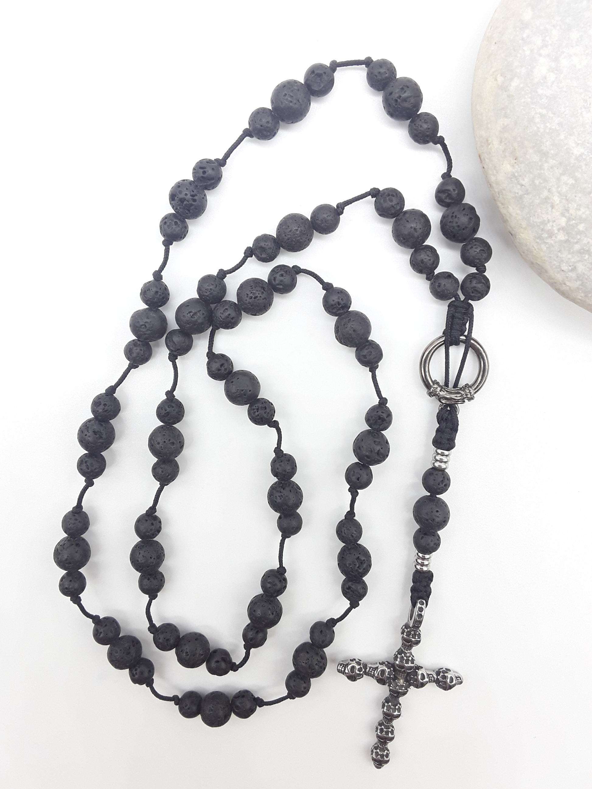 Catholic lava stone rosary with skull crucifix placed beside natural stone on white surface