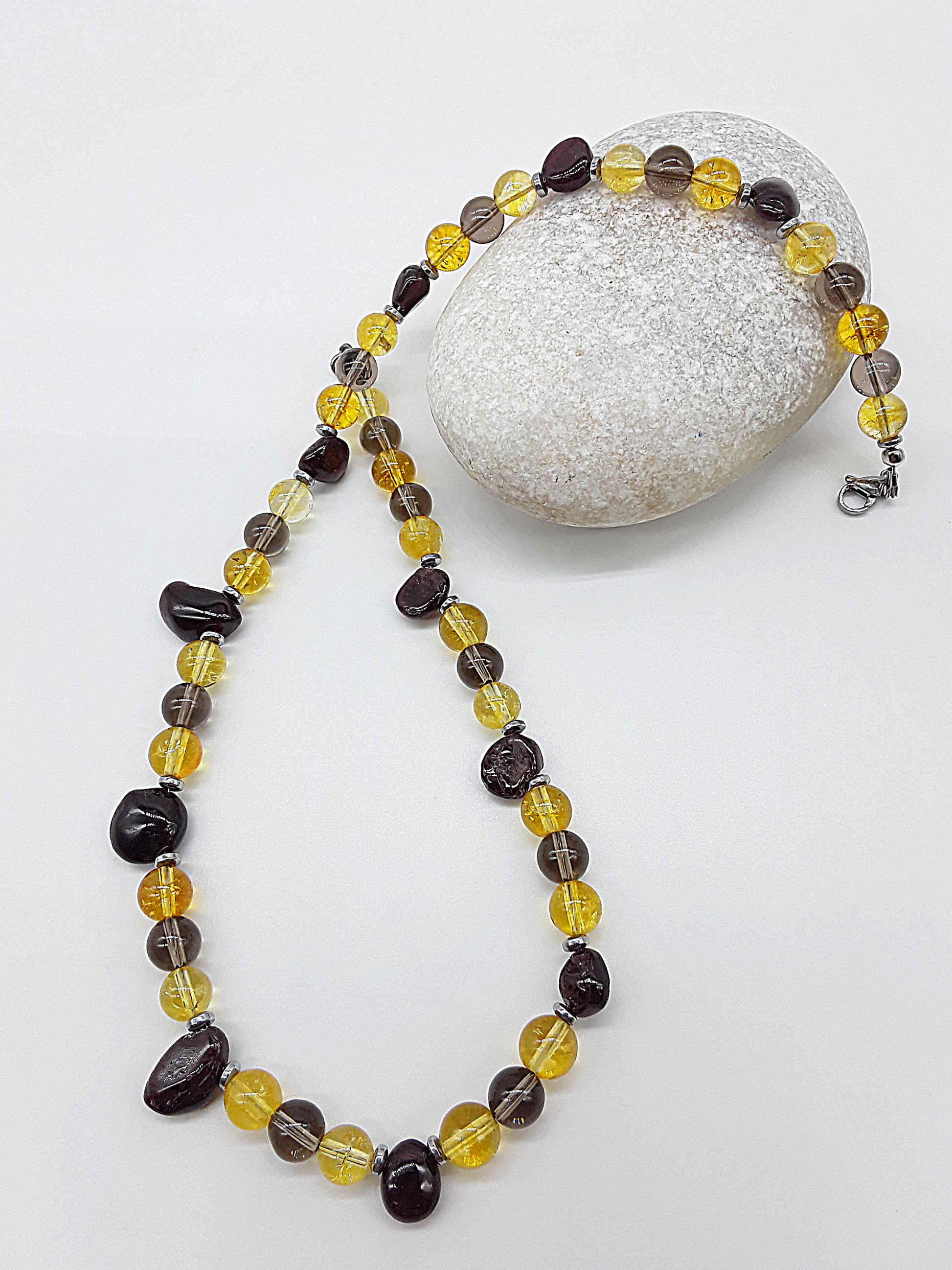 Yellow citrine, dark garnet, smoked quartz, and hematite beaded necklace styled next to a white decorative stone.