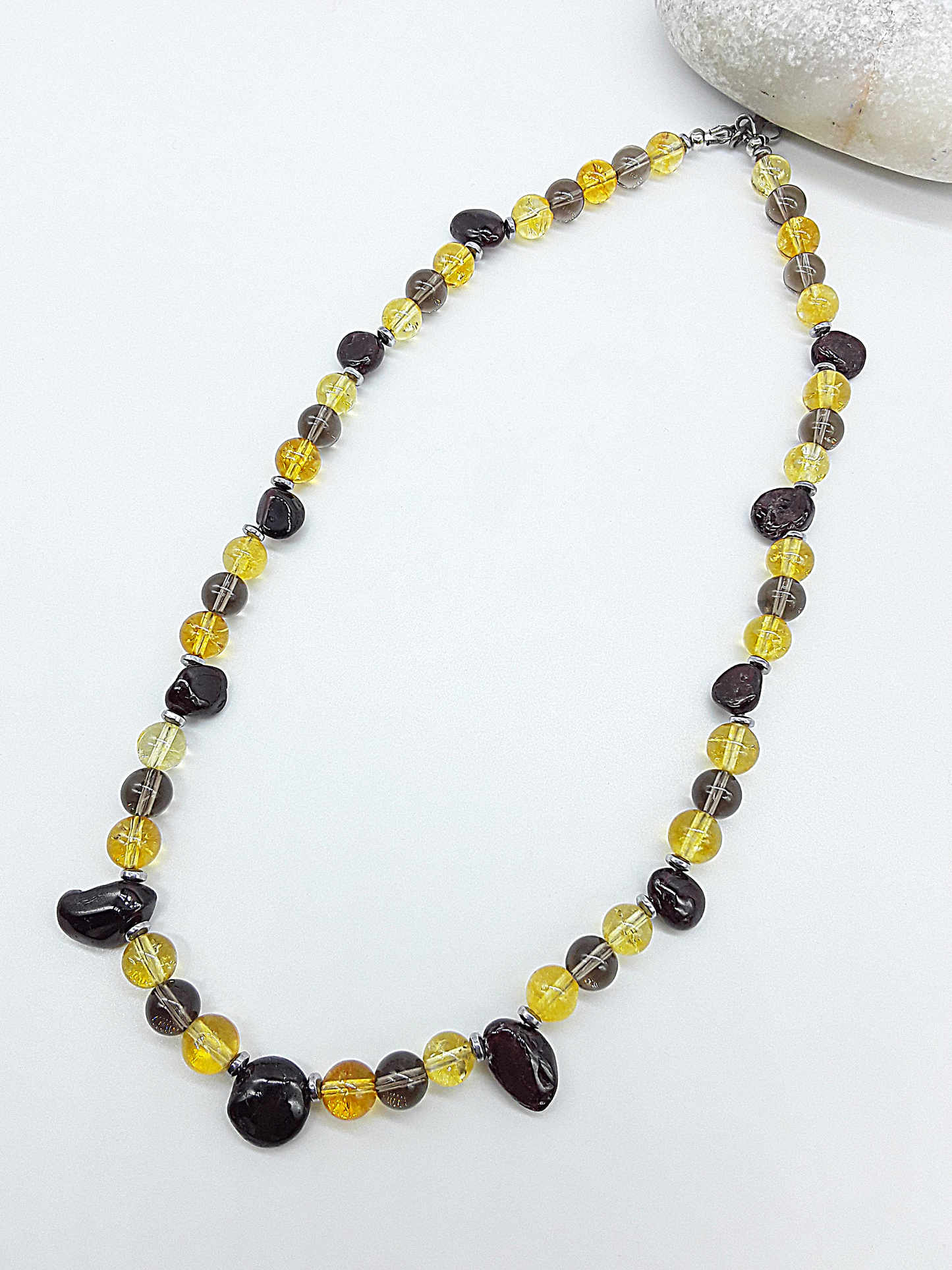 Yellow citrine, dark garnet, smoked quartz, and hematite beaded necklace styled next to a white decorative stone.