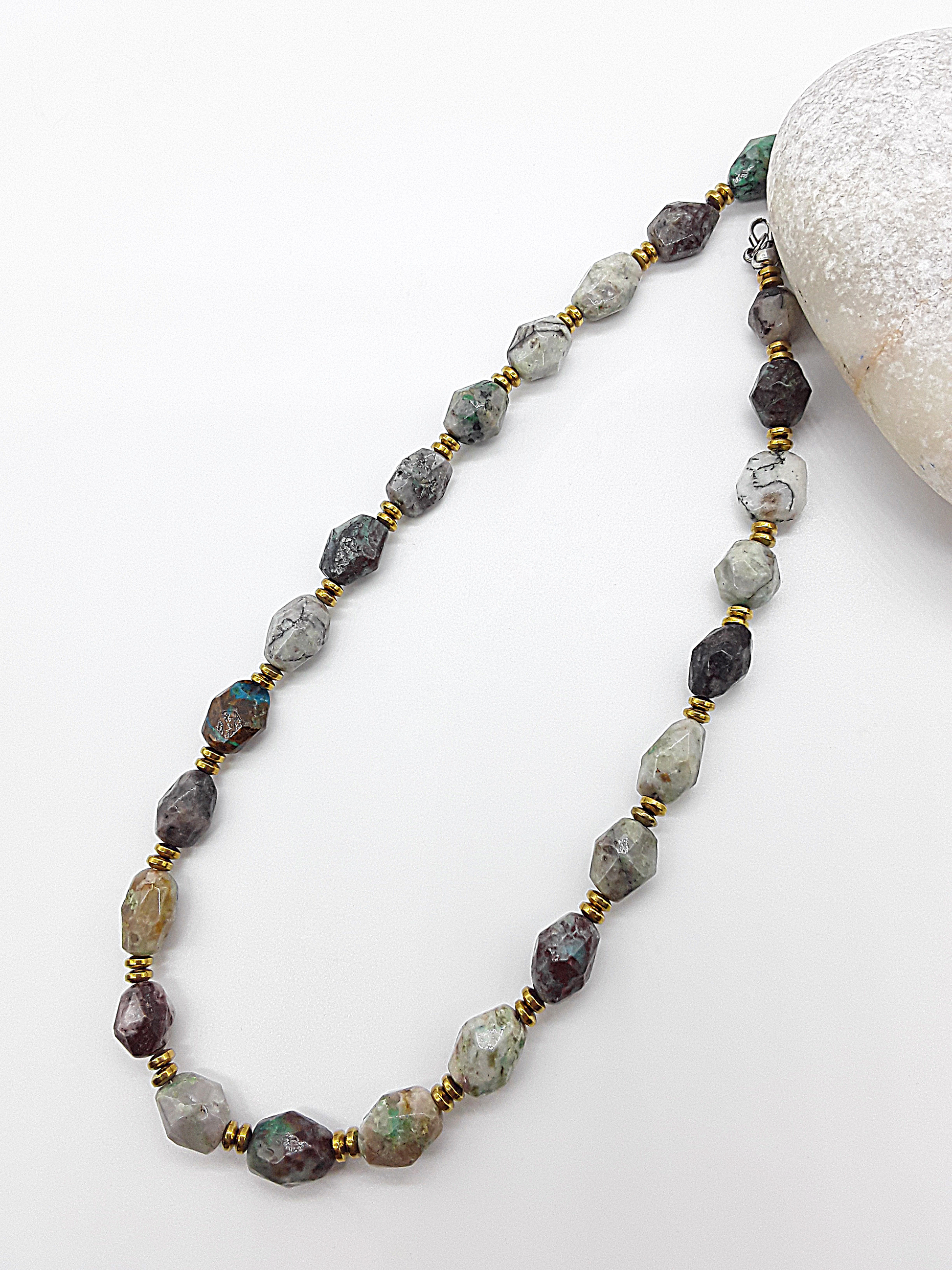 Natural stone necklace with multicolored faceted beads and gold spacers displayed on a white surface next to a smooth white stone.