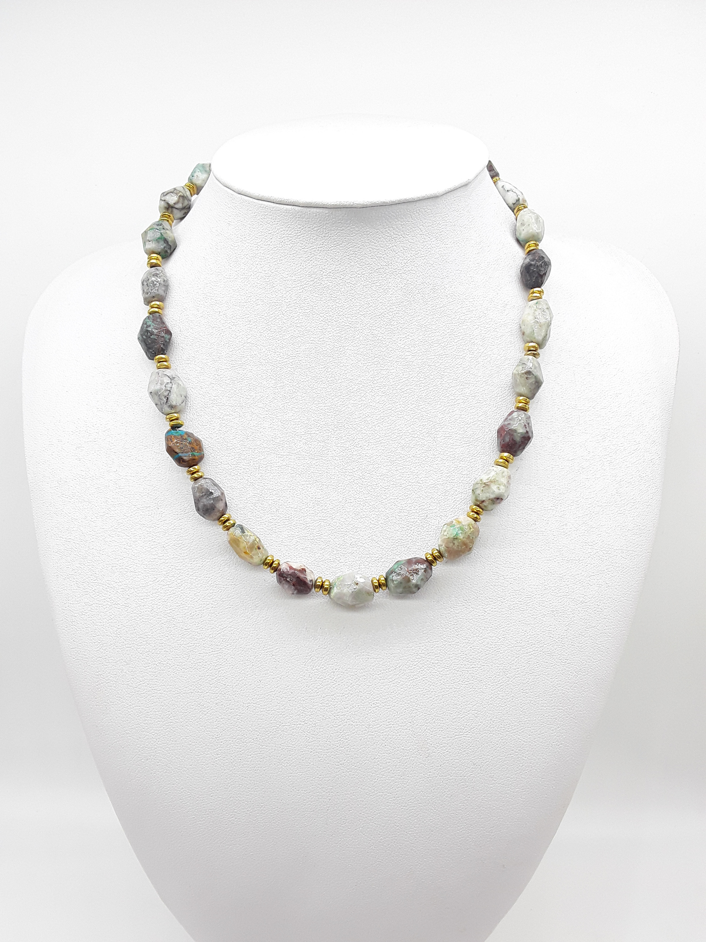 Handcrafted natural stone necklace with multicolored faceted beads and gold spacers displayed on a white mannequin.