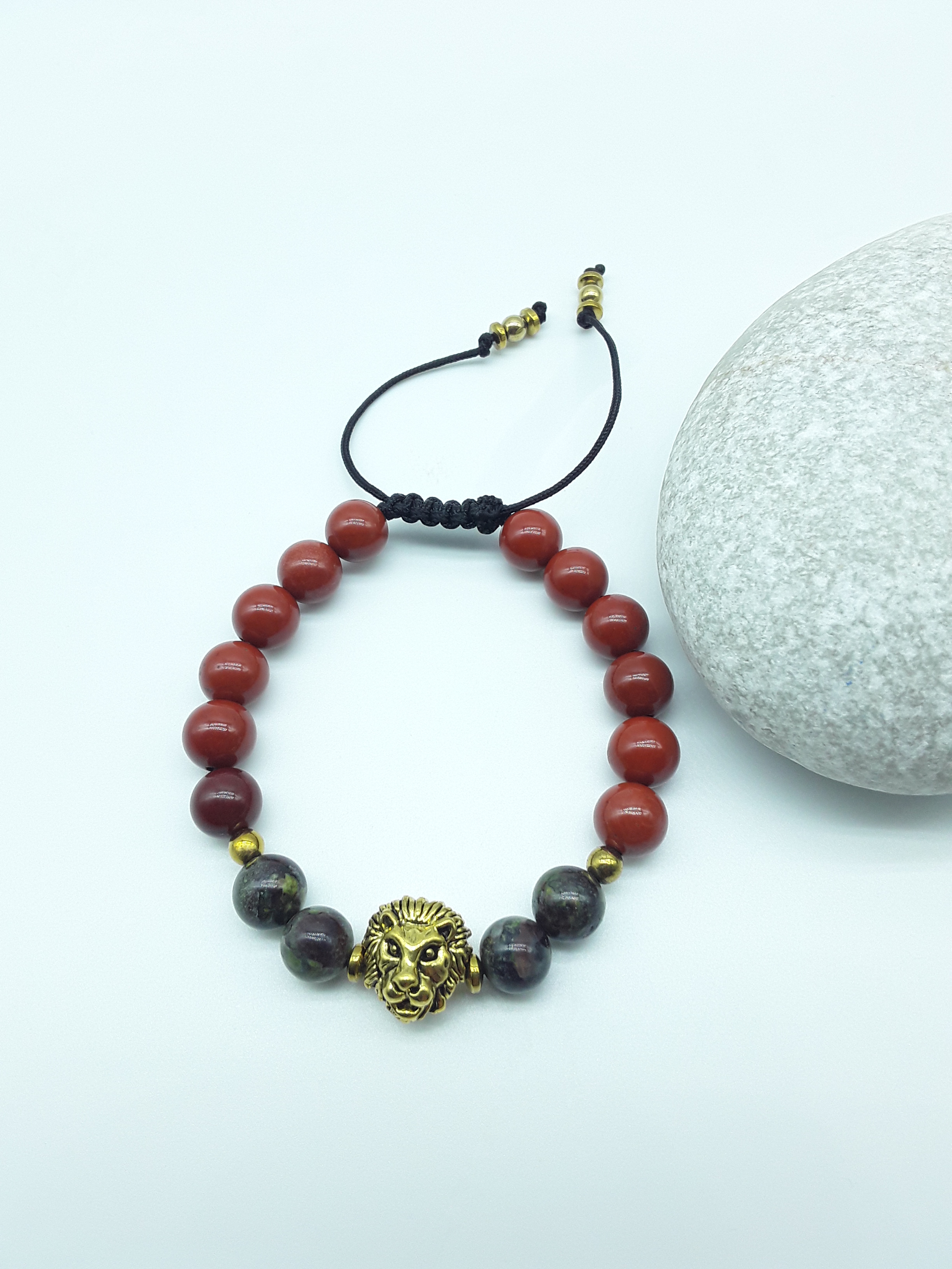 Lion bracelet with red jasper and dragon blood stones placed beside a natural stone